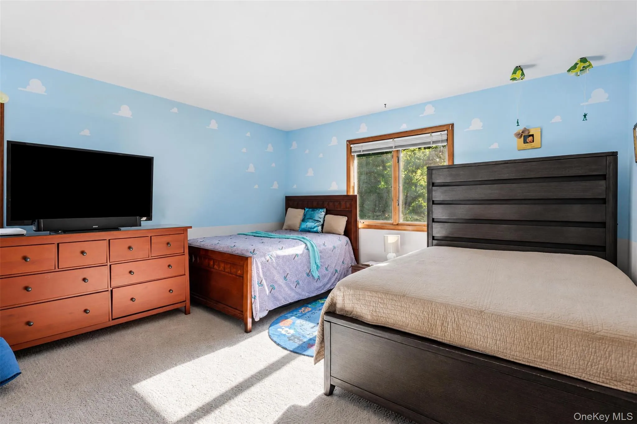 Bedroom featuring light blue walls with cloud detailing, a large window with natural wood trim, and neutral carpet flooring Bedroom featuring light blue walls with cloud detailing, a large window with natural wood trim, and neutral carpet flooring
