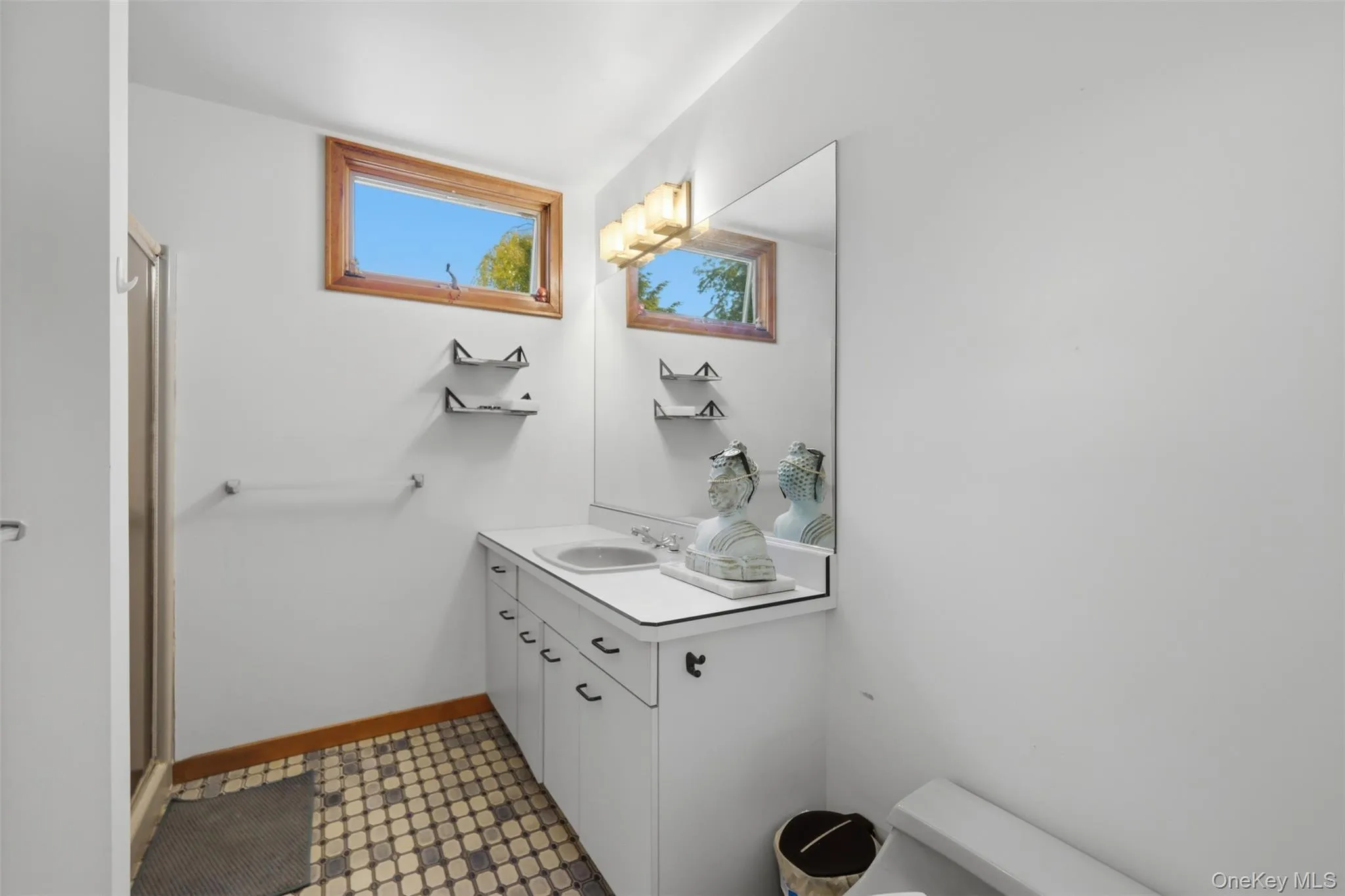 Bathroom with a white vanity featuring integrated sink, large wall mirror, and a three-light vanity fixture Bathroom with a white vanity featuring integrated sink, large wall mirror, and a three-light vanity fixture