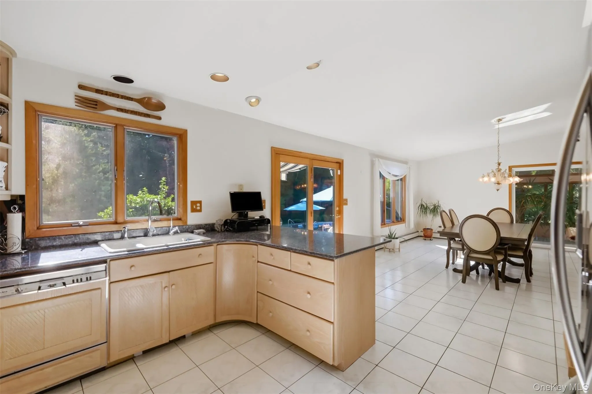 Open-concept kitchen and dining area featuring light wood cabinetry, dark stone countertops, an integrated dishwasher, and tile flooring Open-concept kitchen and dining area featuring light wood cabinetry, dark stone countertops, an integrated dishwasher, and tile flooring