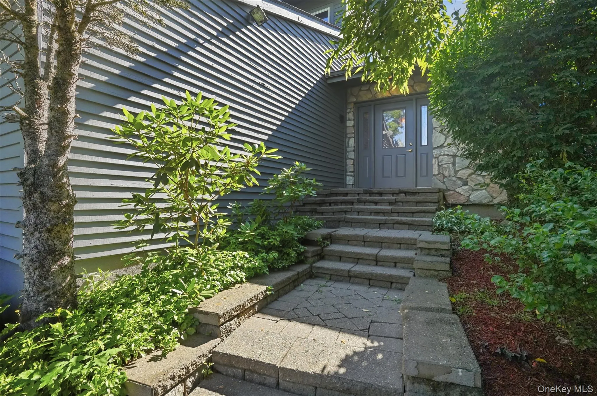 Stone paver walkway with retaining wall steps leading to a gray entry door Stone paver walkway with retaining wall steps leading to a gray entry door