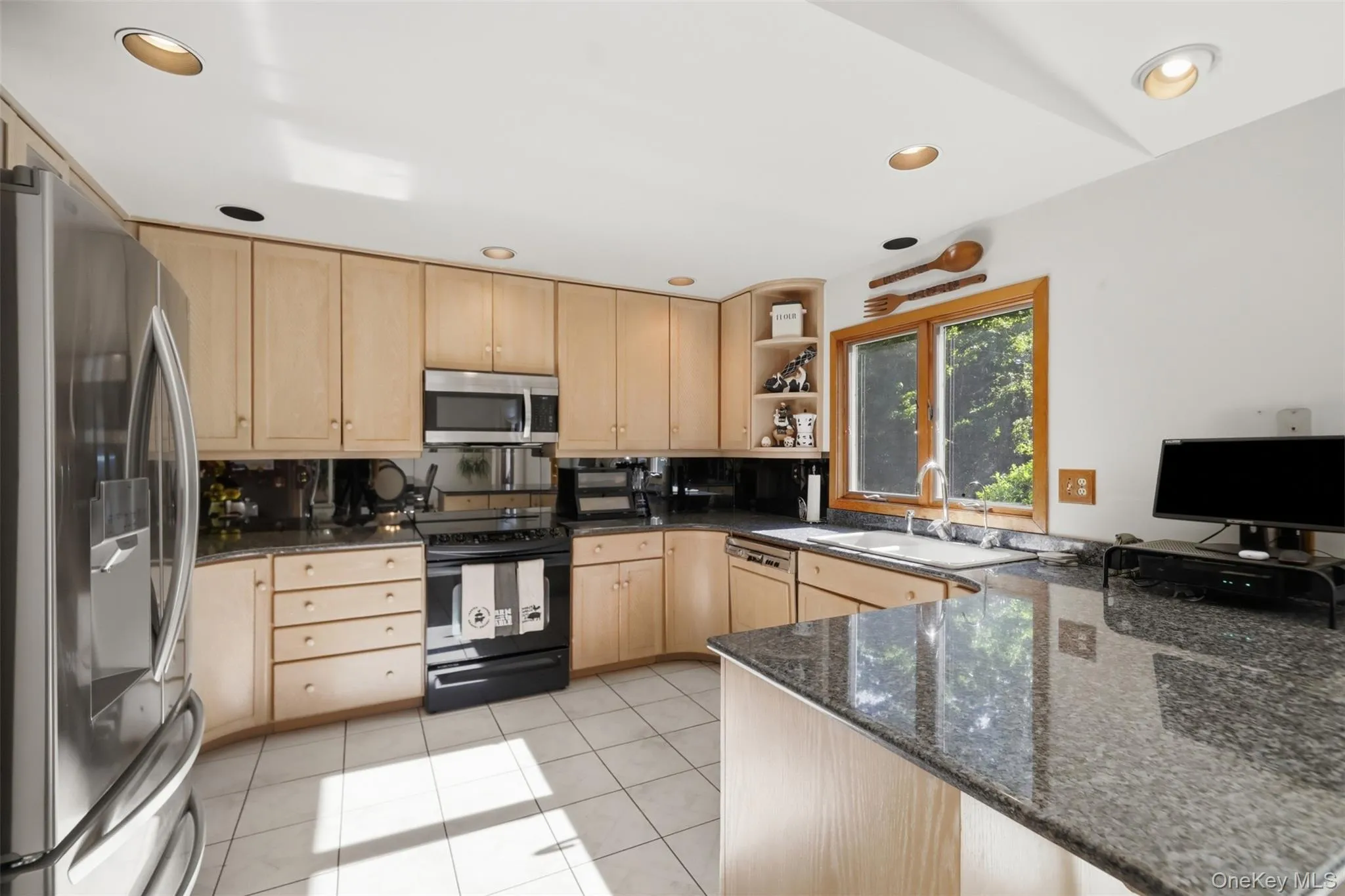 Kitchen featuring light wood cabinetry, stainless steel refrigerator, black range, and stone countertops Kitchen featuring light wood cabinetry, stainless steel refrigerator, black range, and stone countertops