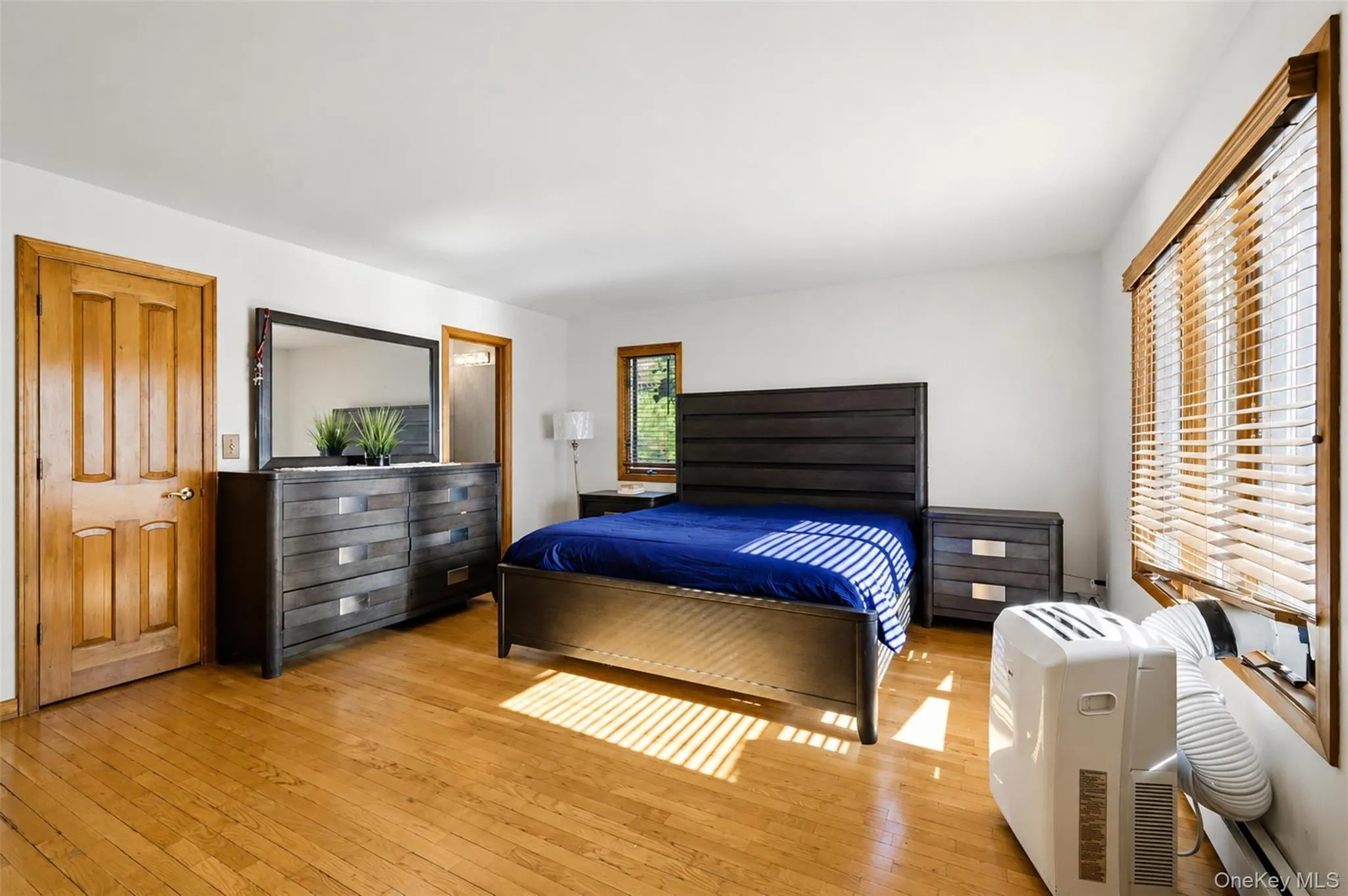 Hardwood flooring enhancing a room with white walls, a multi-paneled wood door, and a window featuring wood-slat blinds Hardwood flooring enhancing a room with white walls, a multi-paneled wood door, and a window featuring wood-slat blinds