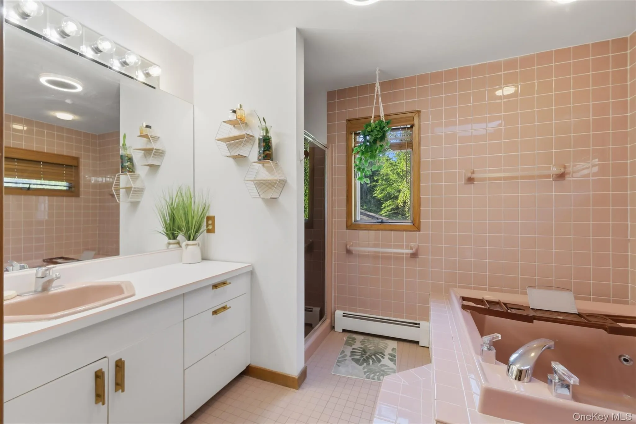 Bathroom featuring a pink tiled shower surround, a built-in jetted tub with integrated shelving, and a vanity with a drop-in sink Bathroom featuring a pink tiled shower surround, a built-in jetted tub with integrated shelving, and a vanity with a drop-in sink