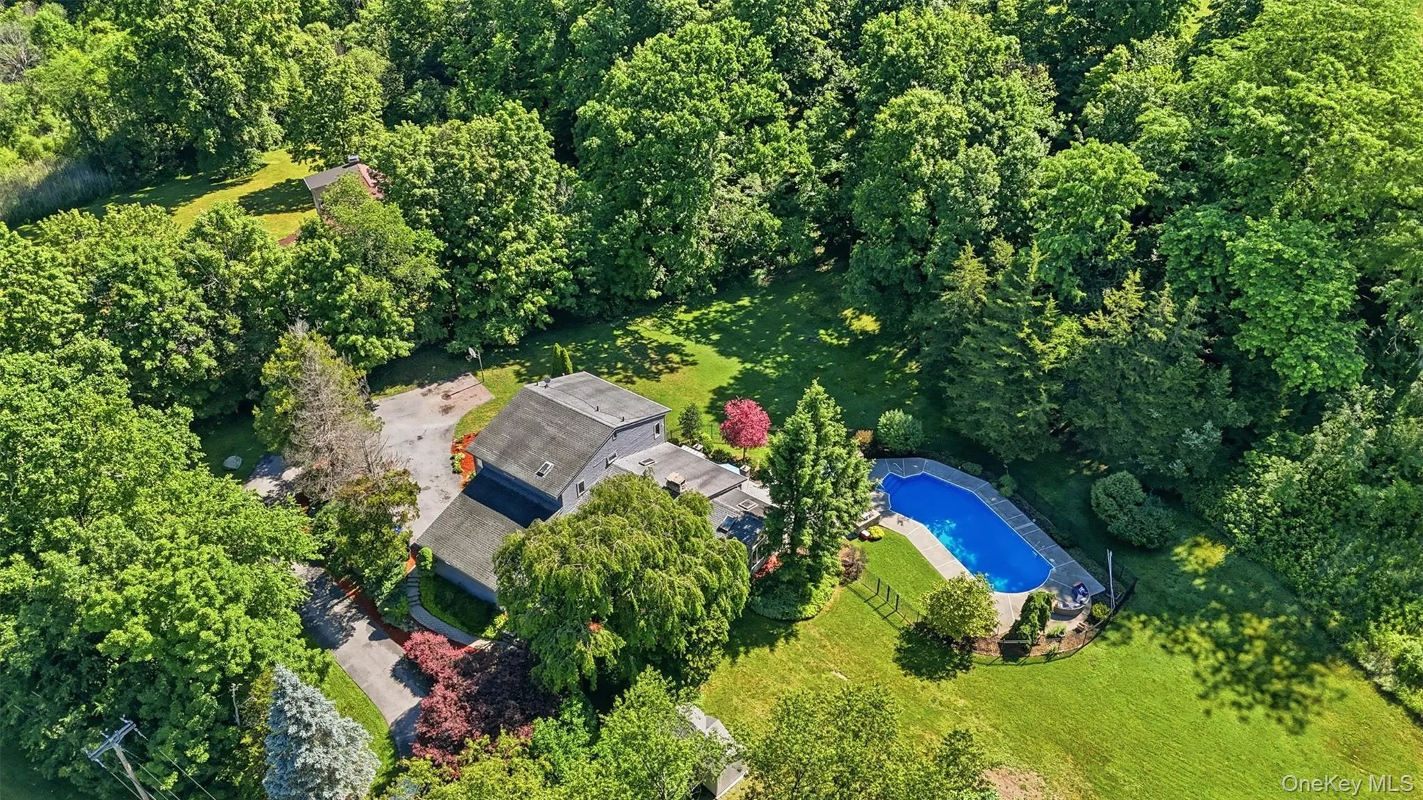 Expansive property featuring a private swimming pool, mature trees, a multi-level residence with a gray exterior, and surrounding green lawn Expansive property featuring a private swimming pool, mature trees, a multi-level residence with a gray exterior, and surrounding green lawn