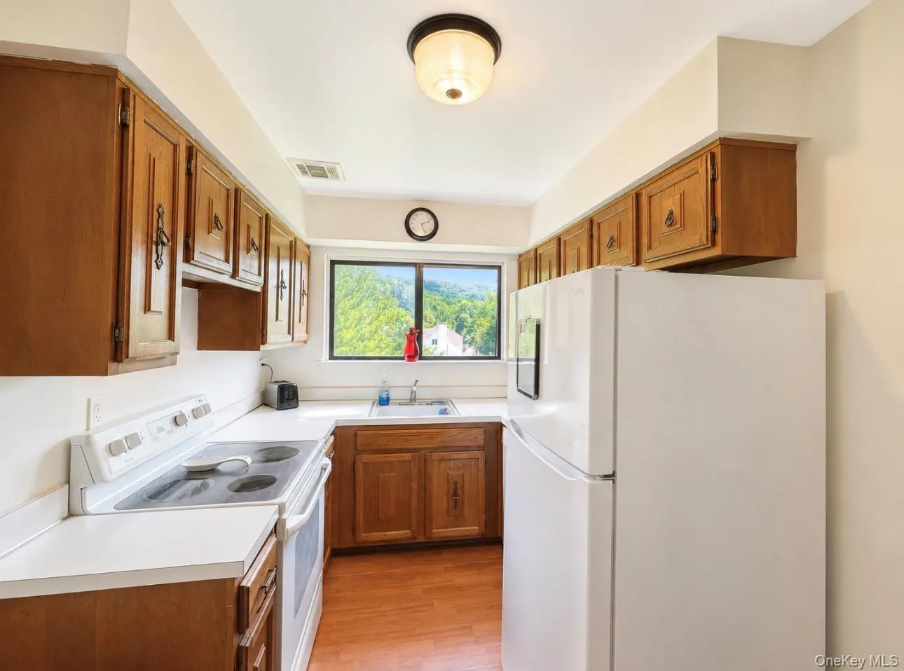 Functional kitchen featuring a window overlooking natural surroundings, wood-finish cabinetry, white countertops, a white electric range, and a white refrigerator Functional kitchen featuring a window overlooking natural surroundings, wood-finish cabinetry, white countertops, a white electric range, and a white refrigerator