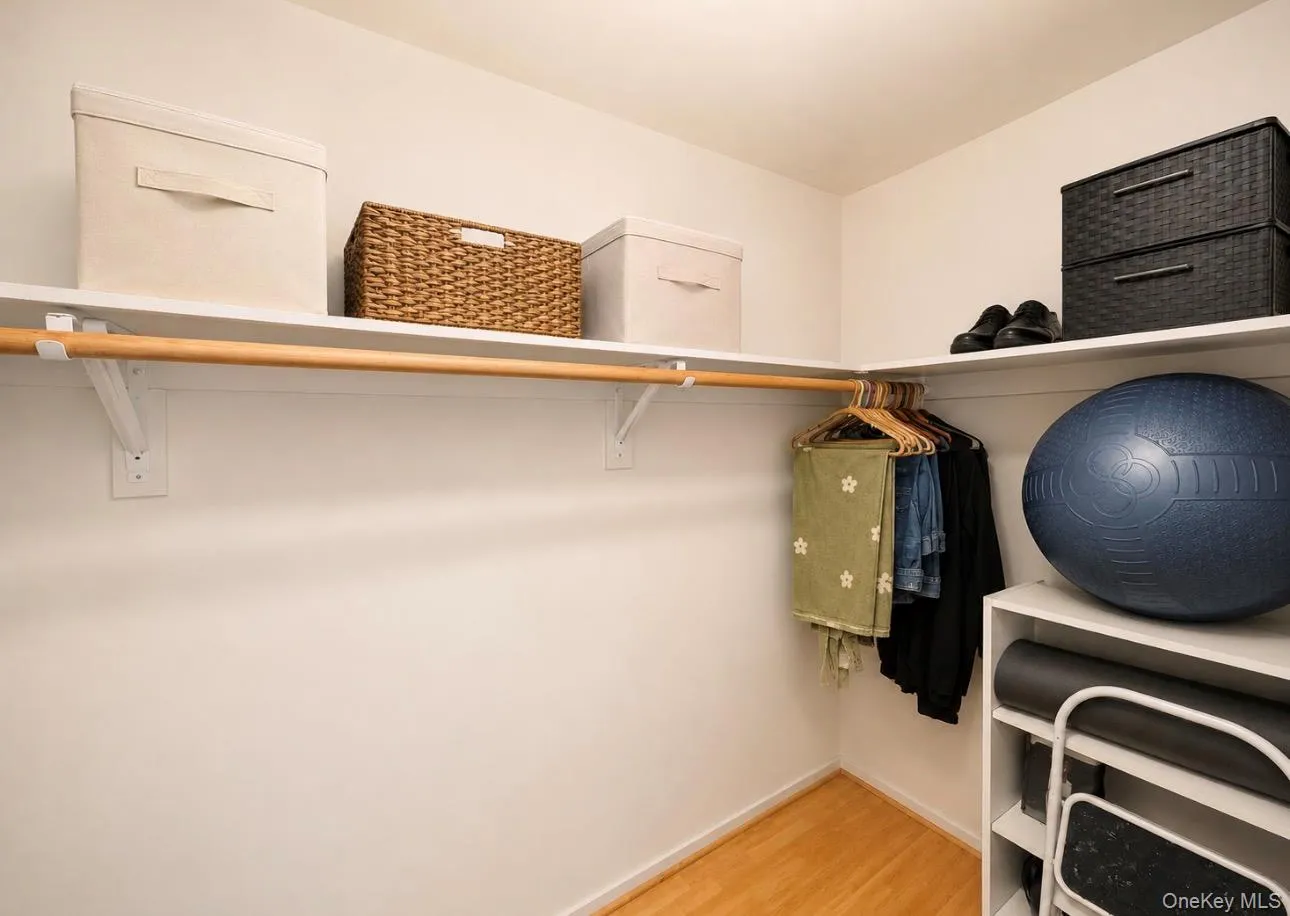 Walk-in closet featuring light wood-finish flooring, white shelving, and a wood hanging rod Walk-in closet featuring light wood-finish flooring, white shelving, and a wood hanging rod