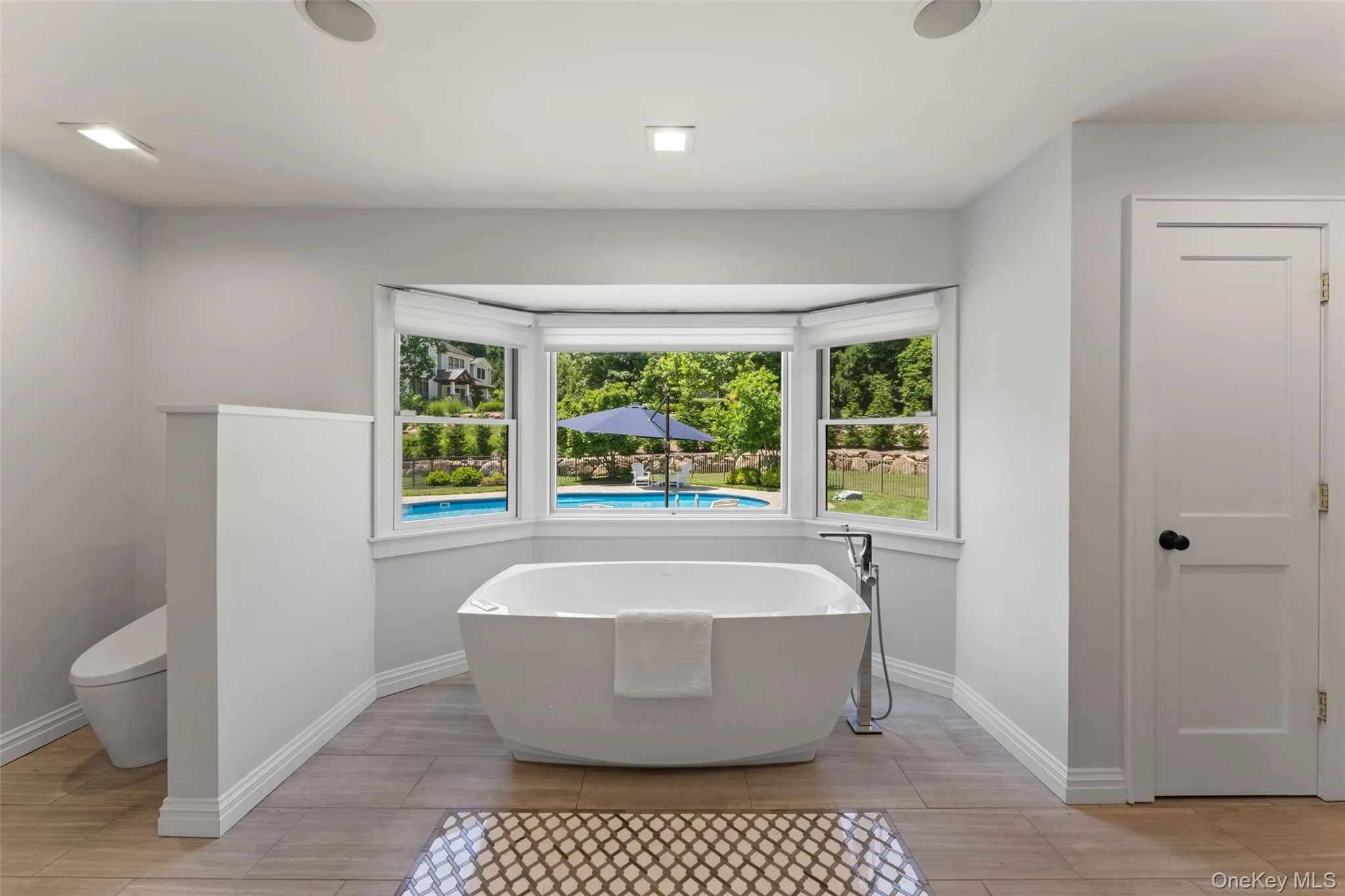Primary ensuite spa-like bath featuring a soaking tub with a view of the pool, steam shower, double vanities, and radiant heated flooring. Primary ensuite spa-like bath featuring a soaking tub with a view of the pool, steam shower, double vanities, and radiant heated flooring.