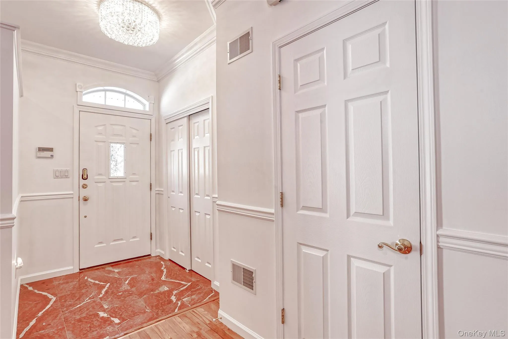Entryway with ornamental molding, visible vents, light wood finished floors, and an inviting chandelier Entryway with ornamental molding, visible vents, light wood finished floors, and an inviting chandelier