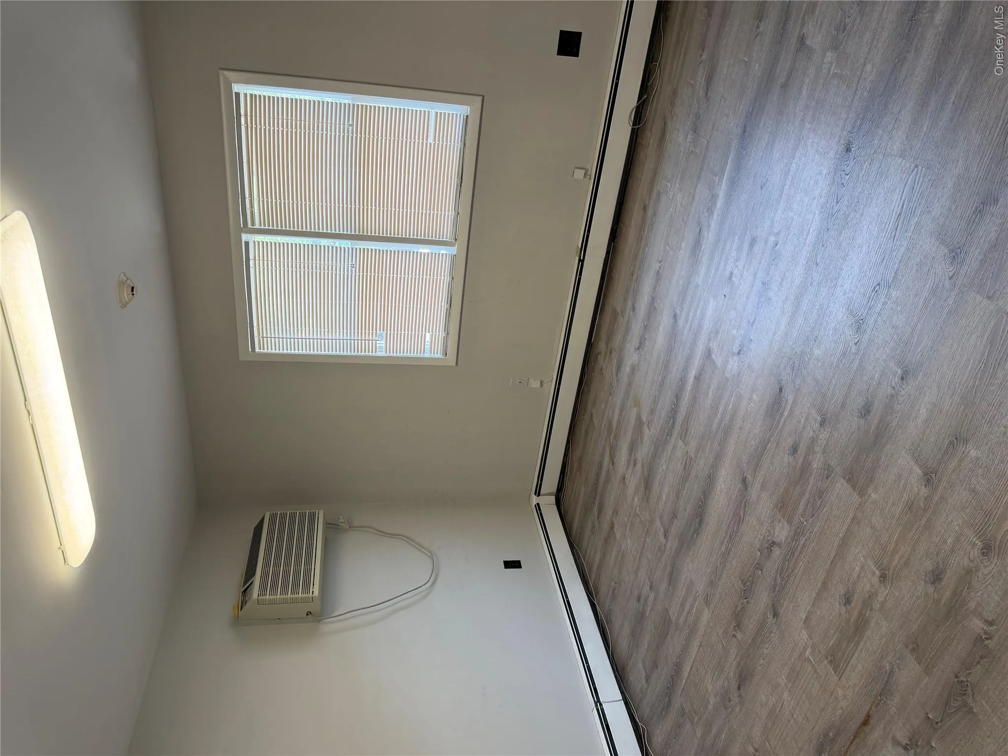 Room featuring wood-finish flooring, a window with blinds, and white baseboard heating Room featuring wood-finish flooring, a window with blinds, and white baseboard heating