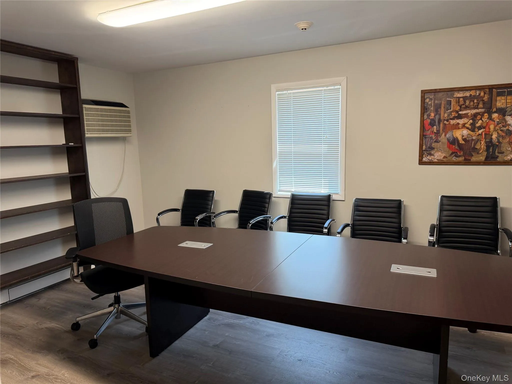 Conference room featuring a large rectangular table with built-in power outlets, wall-mounted air conditioning unit, window with horizontal blinds, and wood-finish flooring Conference room featuring a large rectangular table with built-in power outlets, wall-mounted air conditioning unit, window with horizontal blinds, and wood-finish flooring