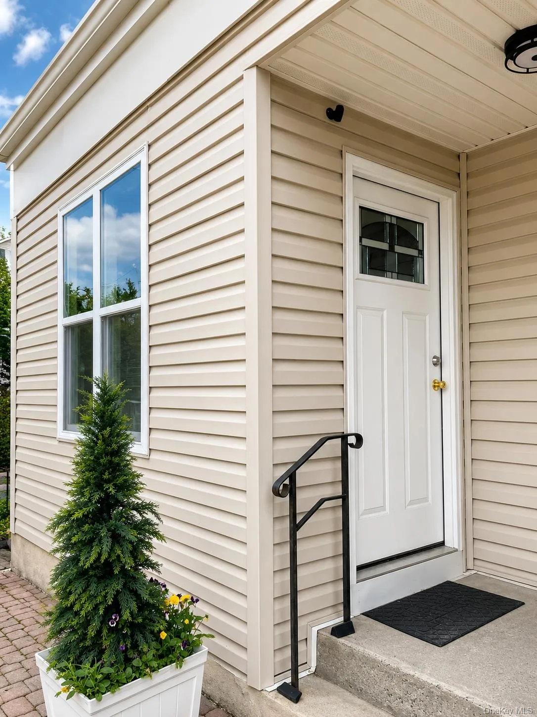 Neutral-toned horizontal siding exterior featuring a white entry door with decorative glass, a concrete stoop with a black metal handrail, and a double-pane window Neutral-toned horizontal siding exterior featuring a white entry door with decorative glass, a concrete stoop with a black metal handrail, and a double-pane window
