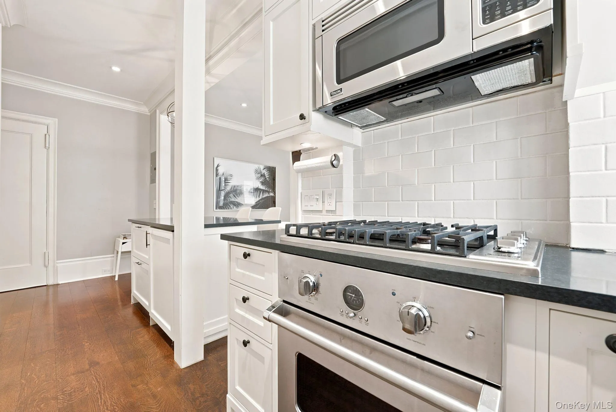 Stainless steel gas range with coordinating microwave and hood, complemented by a white subway tile backsplash, dark countertops, and white cabinetry Stainless steel gas range with coordinating microwave and hood, complemented by a white subway tile backsplash, dark countertops, and white cabinetry