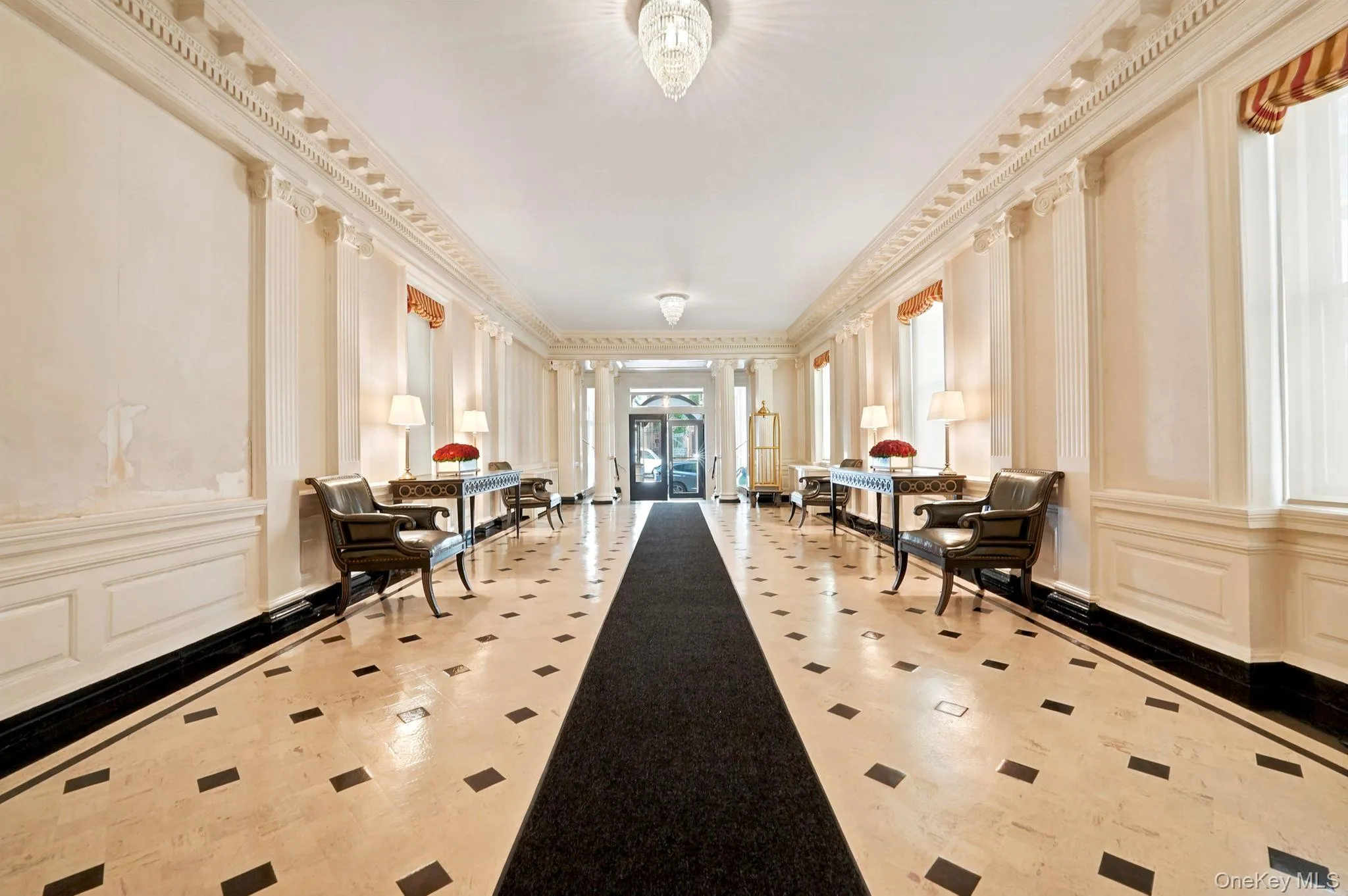 Hallway featuring stone tile flooring with contrasting accents, decorative wall paneling, and architectural columns Hallway featuring stone tile flooring with contrasting accents, decorative wall paneling, and architectural columns