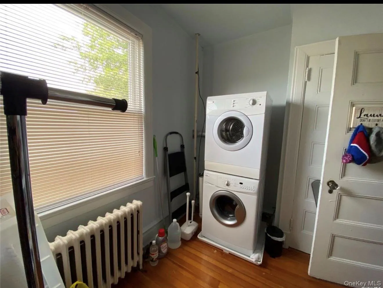 Dedicated laundry area featuring a stacked washer and dryer unit, hardwood-finish flooring, and a large window with blinds Dedicated laundry area featuring a stacked washer and dryer unit, hardwood-finish flooring, and a large window with blinds
