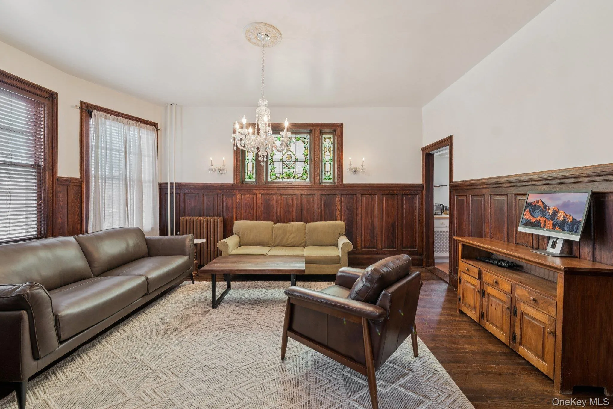 Living area with a wainscoted wall, dark wood finished floors, a chandelier, healthy amount of natural light, and radiator heating unit Living area with a wainscoted wall, dark wood finished floors, a chandelier, healthy amount of natural light, and radiator heating unit