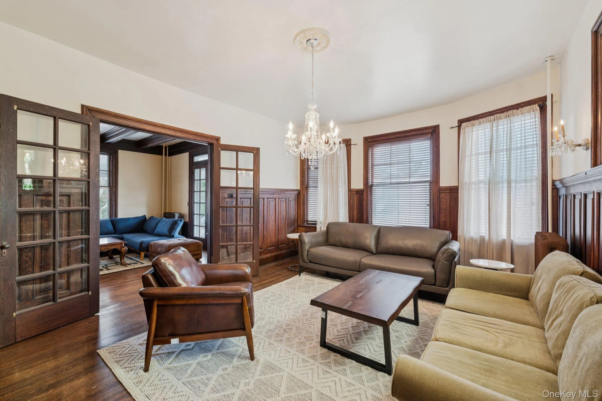 Living room featuring a wainscoted wall, a chandelier, wood finished floors, and french doors Living room featuring a wainscoted wall, a chandelier, wood finished floors, and french doors