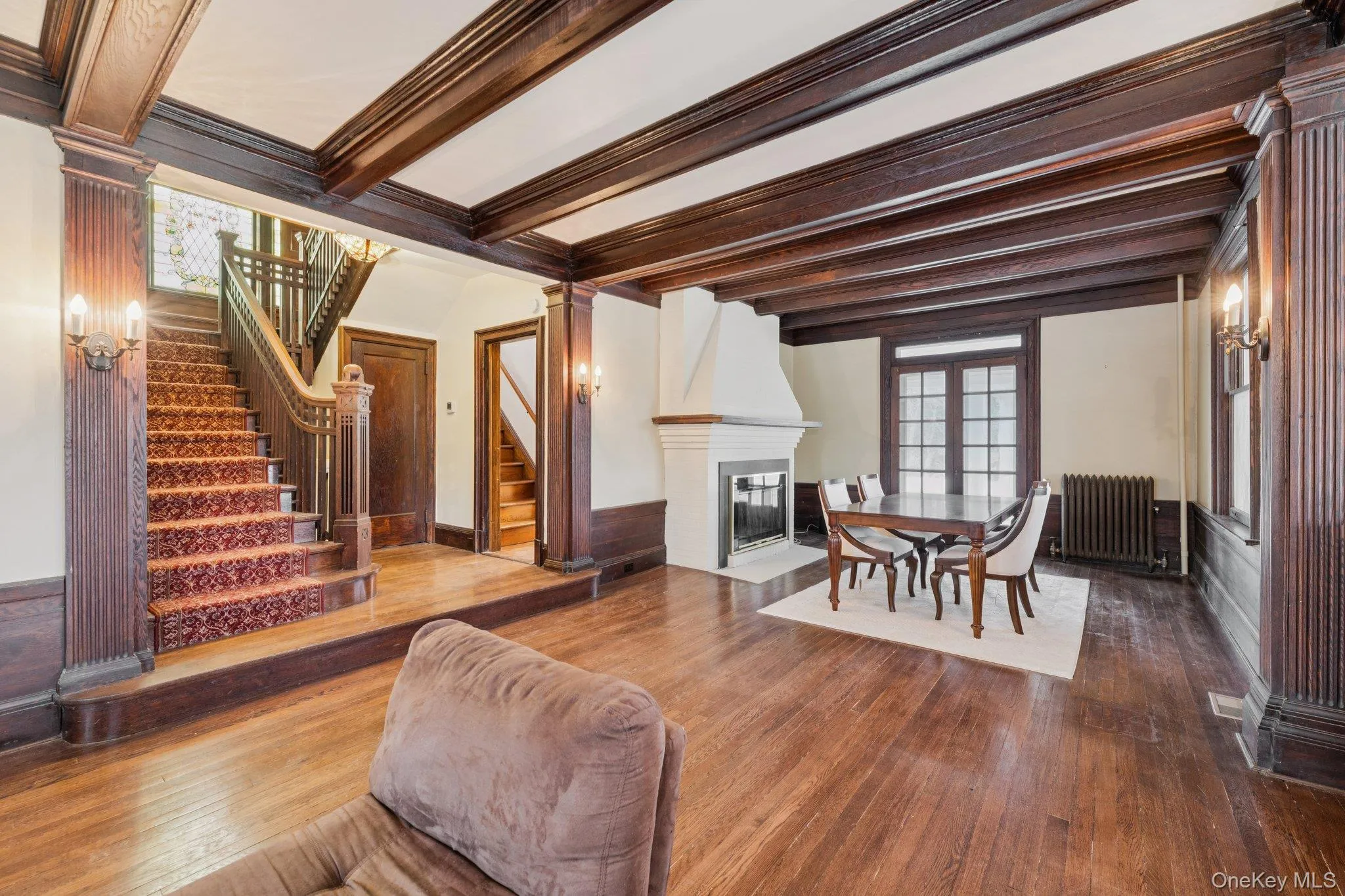 Living room featuring ornate columns, radiator, beam ceiling, a fireplace with flush hearth, and dark wood finished floors Living room featuring ornate columns, radiator, beam ceiling, a fireplace with flush hearth, and dark wood finished floors