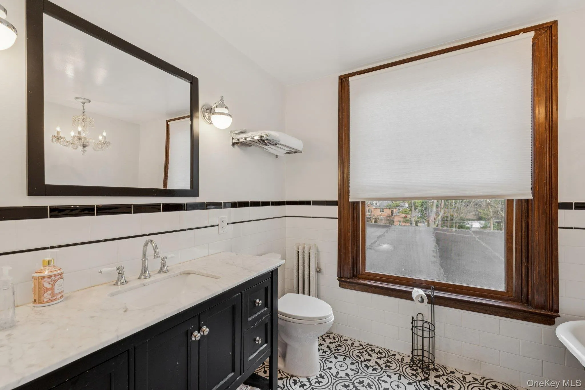 Bathroom with tile walls, radiator heating unit, vanity, a wainscoted wall, and light tile patterned floors Bathroom with tile walls, radiator heating unit, vanity, a wainscoted wall, and light tile patterned floors