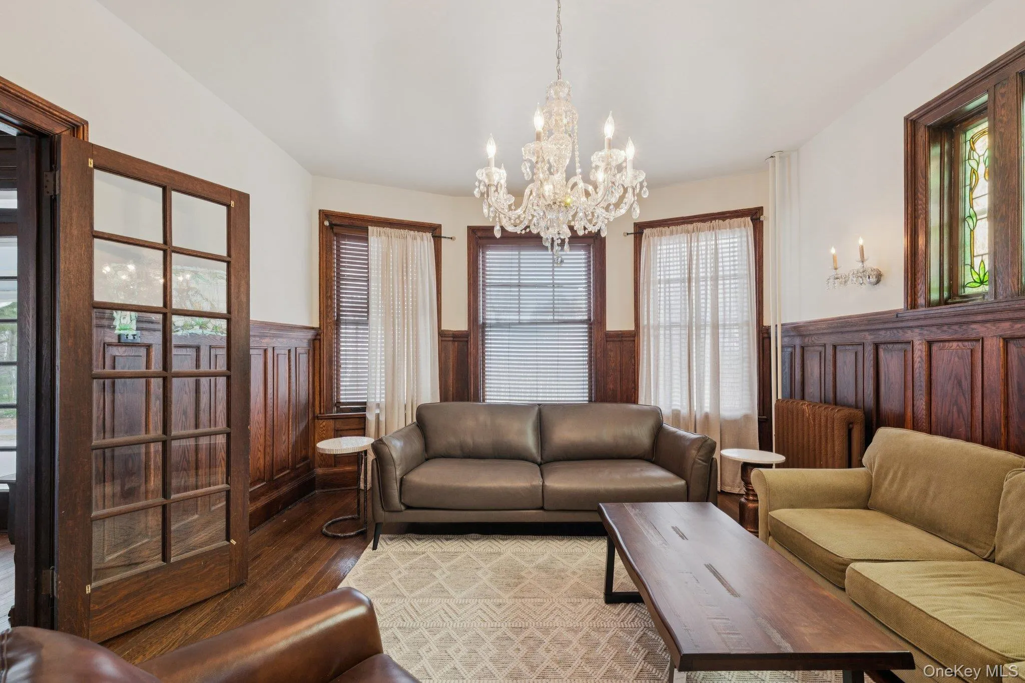 Living room featuring a wainscoted wall, wood finished floors, a chandelier, and radiator Living room featuring a wainscoted wall, wood finished floors, a chandelier, and radiator