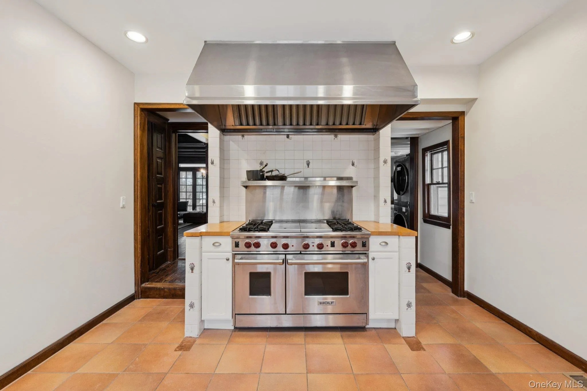 Kitchen with white cabinets, double oven range, ventilation hood, and stacked washing machine and dryer Kitchen with white cabinets, double oven range, ventilation hood, and stacked washing machine and dryer