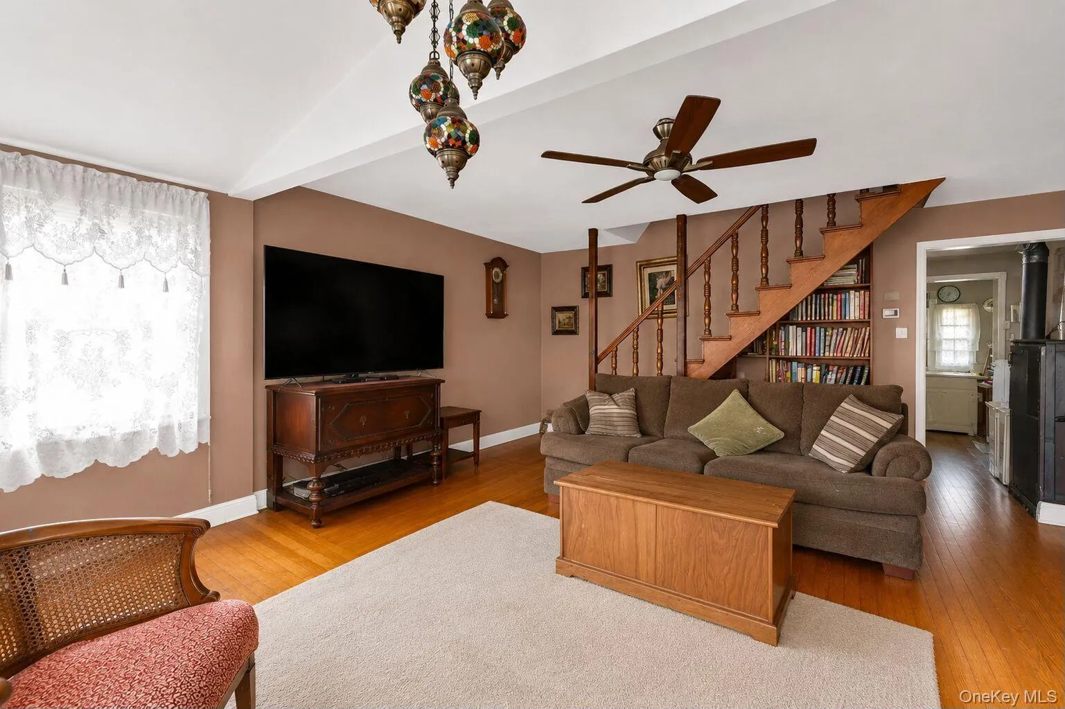 Living area featuring hardwood flooring, a built-in staircase with balusters, recessed built-in shelving, and a ceiling fan Living area featuring hardwood flooring, a built-in staircase with balusters, recessed built-in shelving, and a ceiling fan