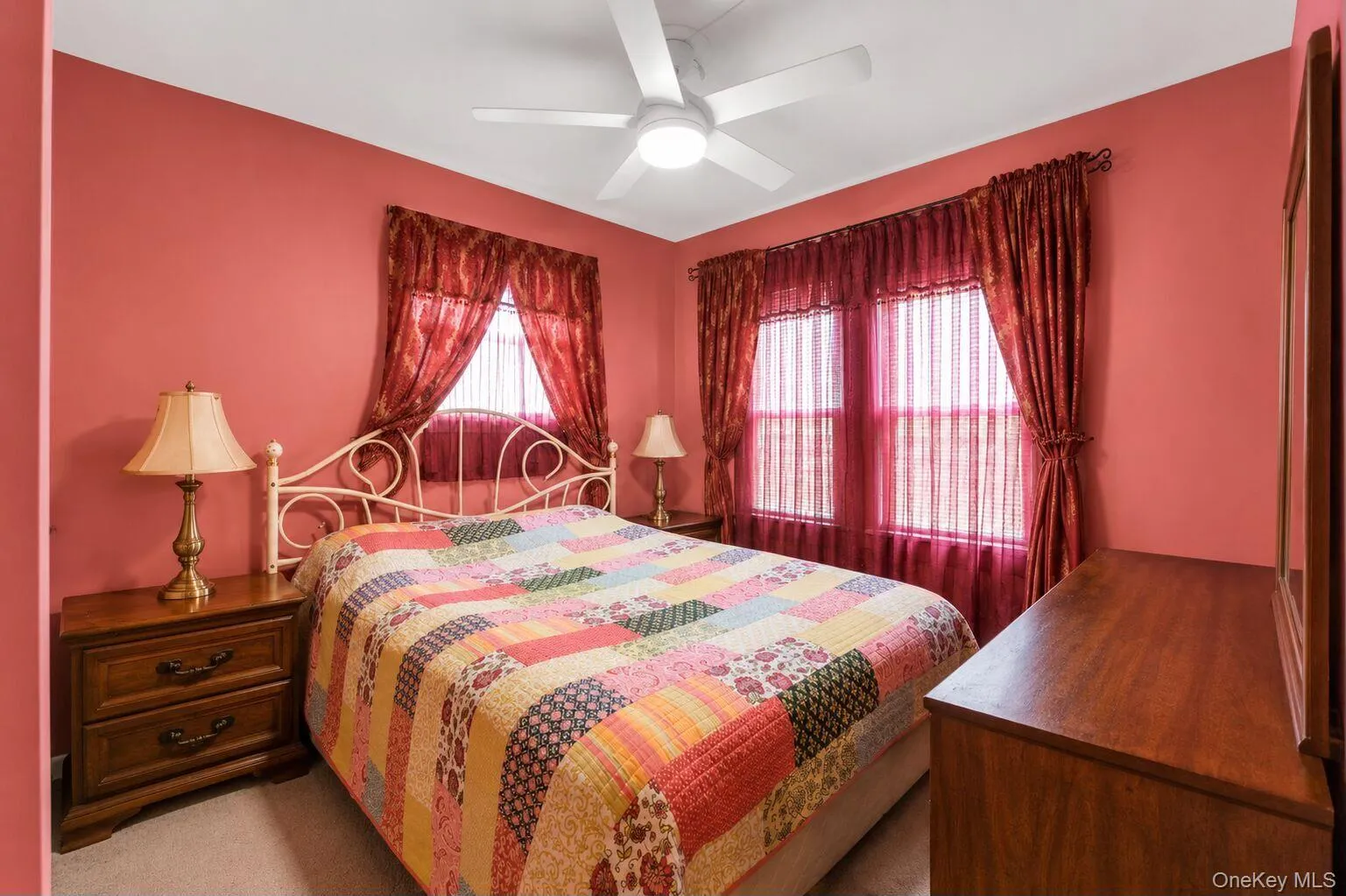 Bedroom featuring two windows with sheer and opaque drapery, a ceiling fan with integrated lighting, and a neutral-toned carpet Bedroom featuring two windows with sheer and opaque drapery, a ceiling fan with integrated lighting, and a neutral-toned carpet
