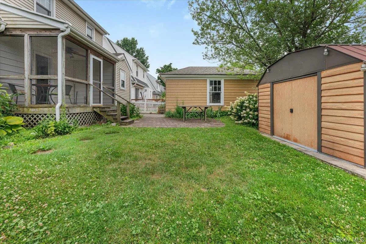 Expansive grassy lawn with a screened porch, a paved patio area, and a separate storage shed featuring wood-finish siding and a metal roof Expansive grassy lawn with a screened porch, a paved patio area, and a separate storage shed featuring wood-finish siding and a metal roof