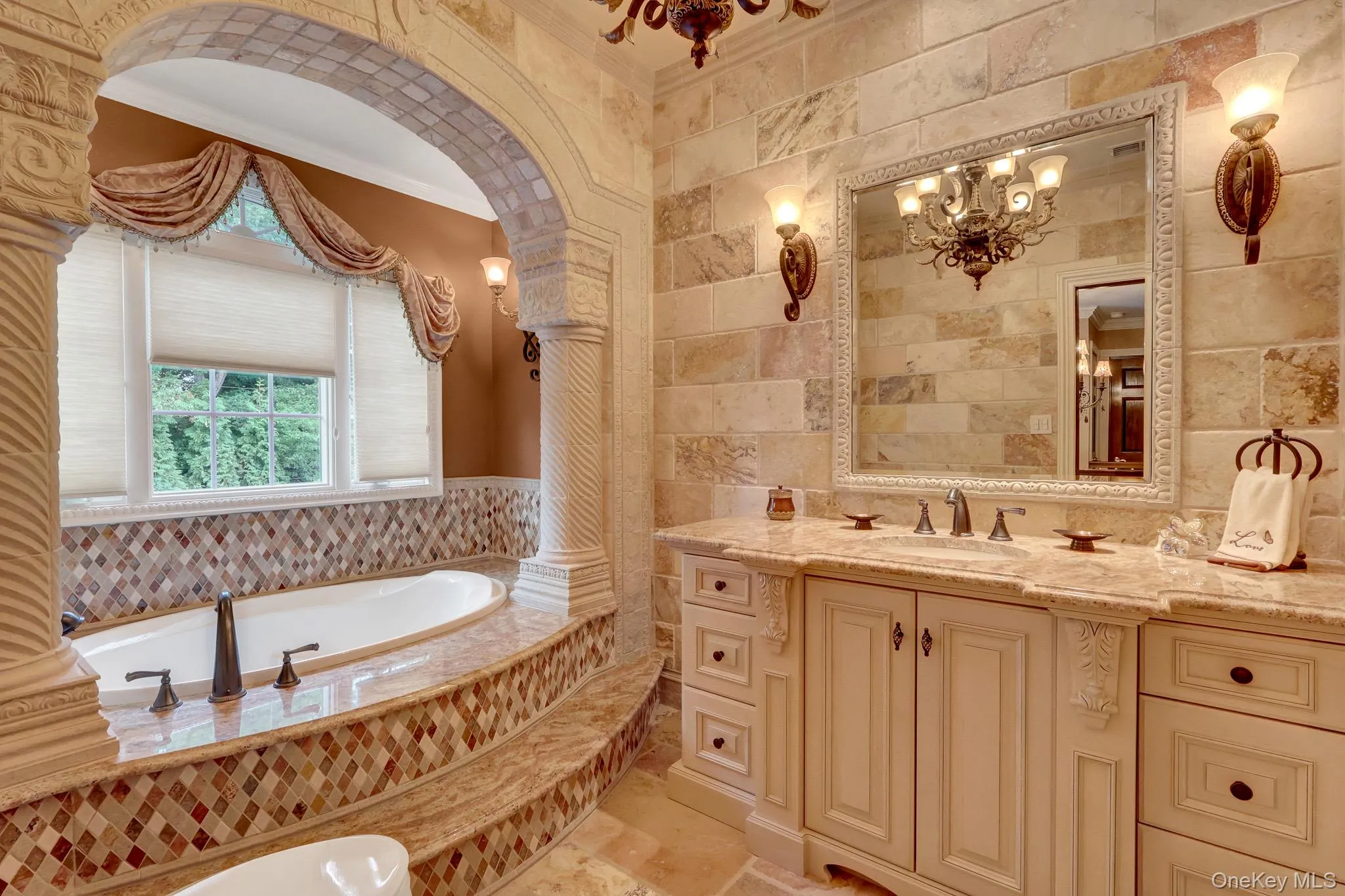 Luxurious bathroom featuring a prominent built-in soaking tub, a double vanity with a light-toned countertop, and decorative architectural details including an arched entryway with fluted columns Luxurious bathroom featuring a prominent built-in soaking tub, a double vanity with a light-toned countertop, and decorative architectural details including an arched entryway with fluted columns