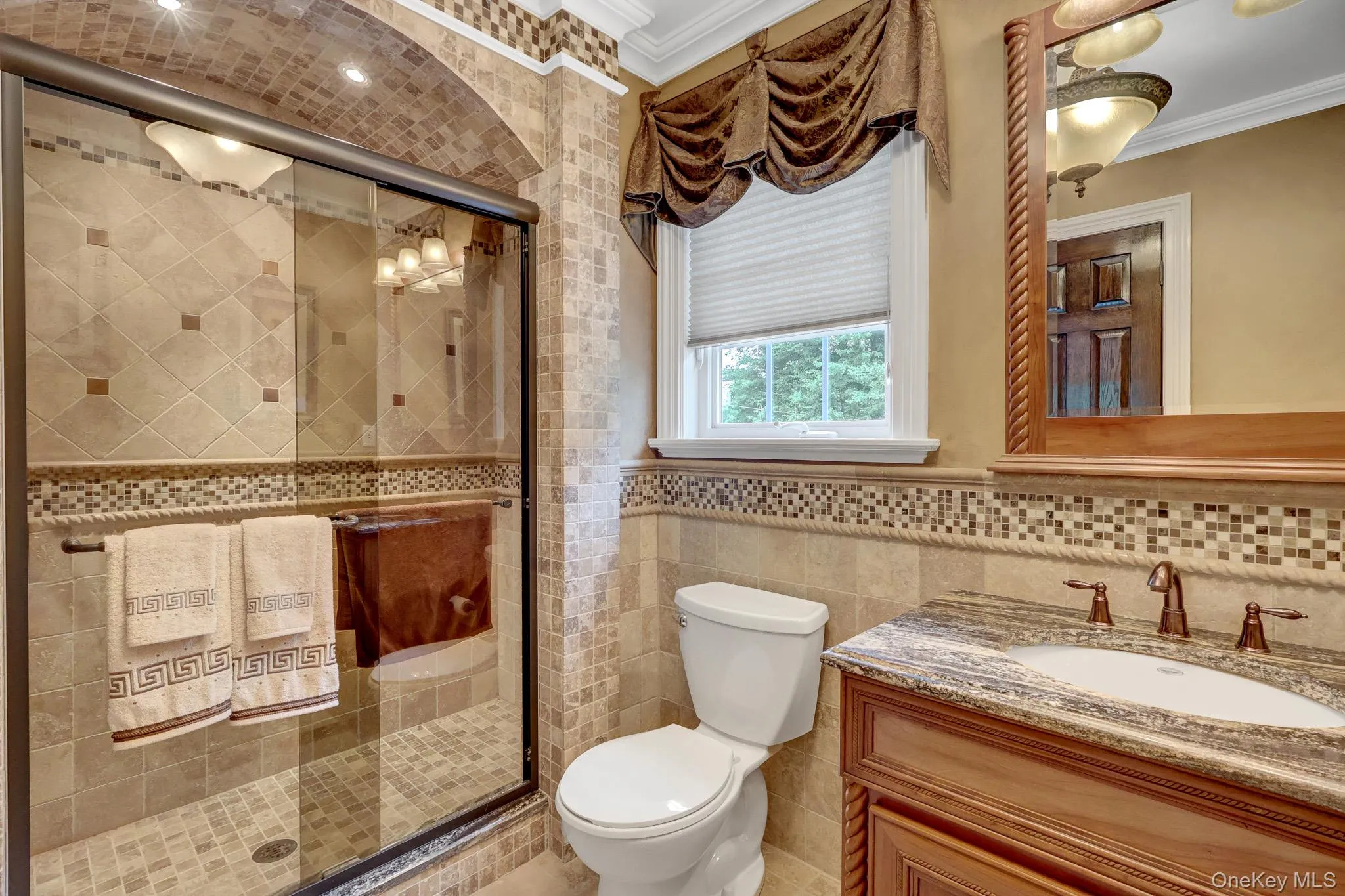 Shower enclosure with clear glass door, floor-to-ceiling tile work, recessed lighting, and a mosaic tile border Shower enclosure with clear glass door, floor-to-ceiling tile work, recessed lighting, and a mosaic tile border