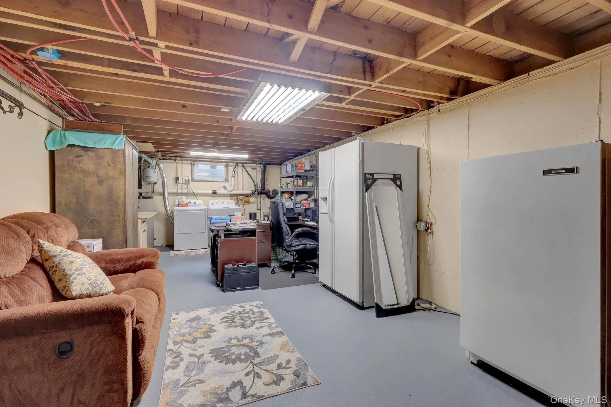 Utility space featuring exposed wood ceiling joists, overhead fluorescent lighting, concrete flooring, and multiple built-in appliances Utility space featuring exposed wood ceiling joists, overhead fluorescent lighting, concrete flooring, and multiple built-in appliances