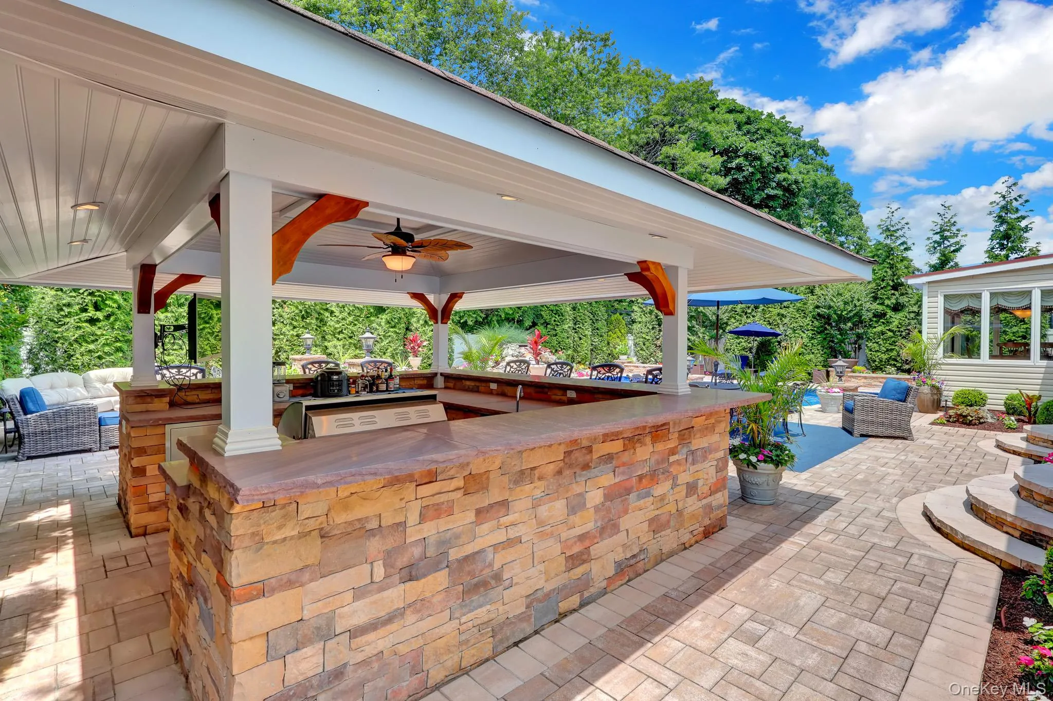Outdoor kitchen with stone veneer base, built-in grill, and a ceiling fan under a covered patio Outdoor kitchen with stone veneer base, built-in grill, and a ceiling fan under a covered patio