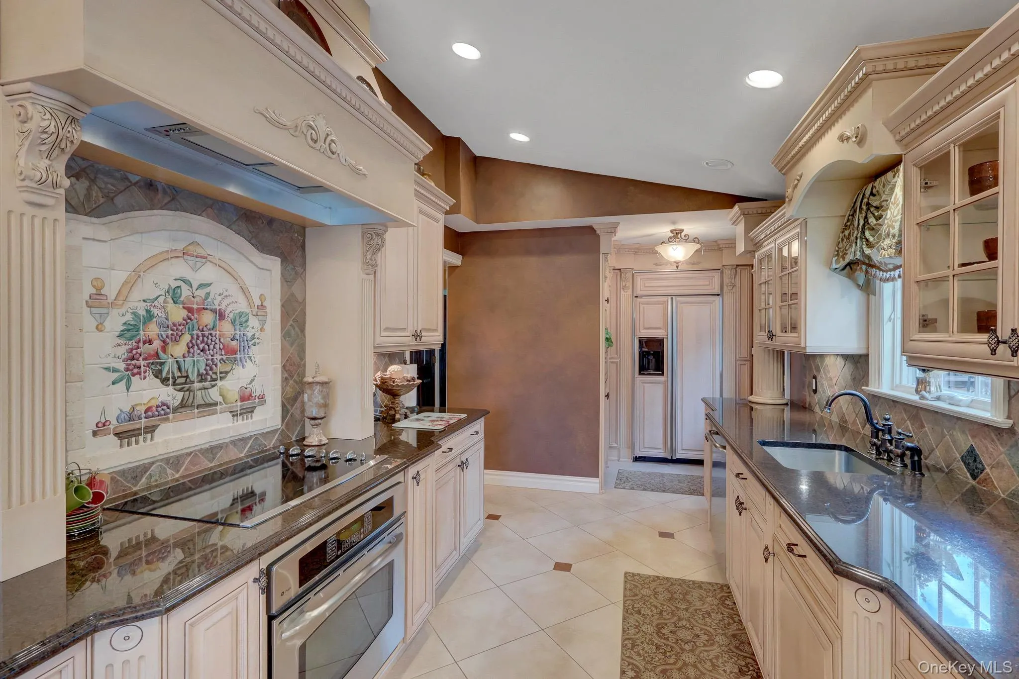 Gourmet kitchen featuring custom cabinetry with ornate detailing, dark stone countertops, and a built-in oven with a cooktop Gourmet kitchen featuring custom cabinetry with ornate detailing, dark stone countertops, and a built-in oven with a cooktop