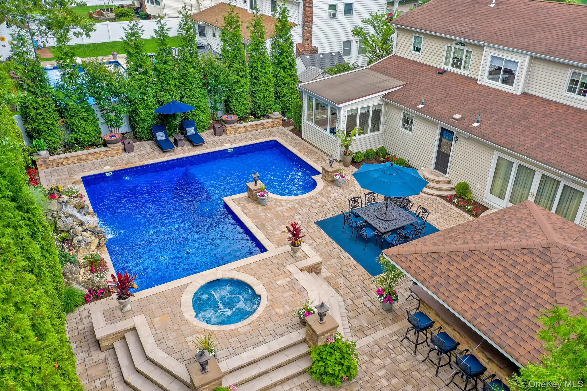 Expansive outdoor entertaining area featuring a large swimming pool with a rock waterfall, an integrated spa, and a built-in bar with seating Expansive outdoor entertaining area featuring a large swimming pool with a rock waterfall, an integrated spa, and a built-in bar with seating