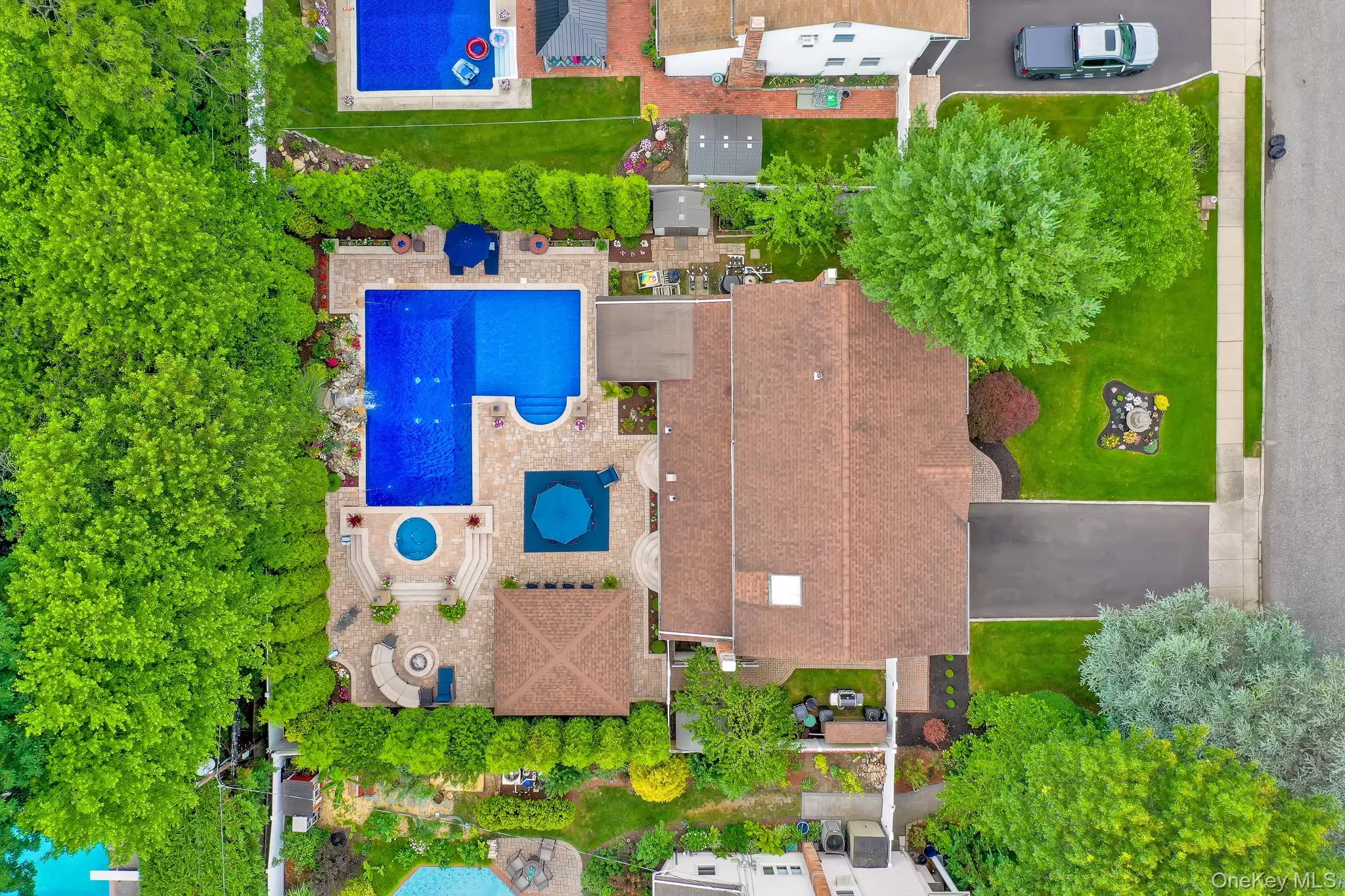 Property featuring a large L-shaped swimming pool with an integrated circular spa, extensive paver patio surround, mature privacy hedging, and a sprawling green lawn Property featuring a large L-shaped swimming pool with an integrated circular spa, extensive paver patio surround, mature privacy hedging, and a sprawling green lawn