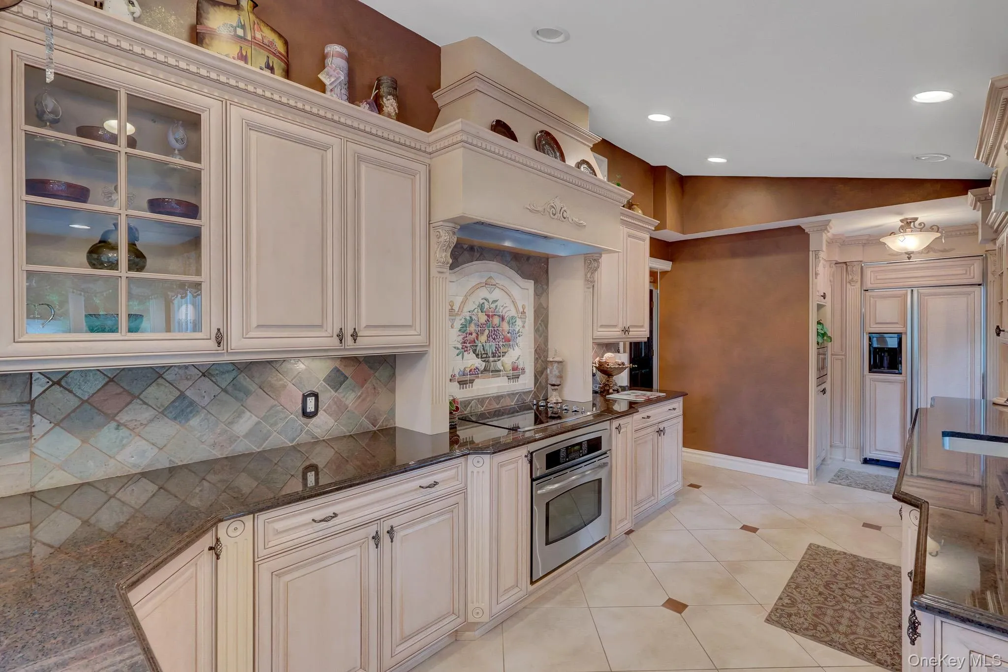 Gourmet kitchen featuring cream-toned cabinetry, dark granite countertops, and a decorative tile backsplash Gourmet kitchen featuring cream-toned cabinetry, dark granite countertops, and a decorative tile backsplash