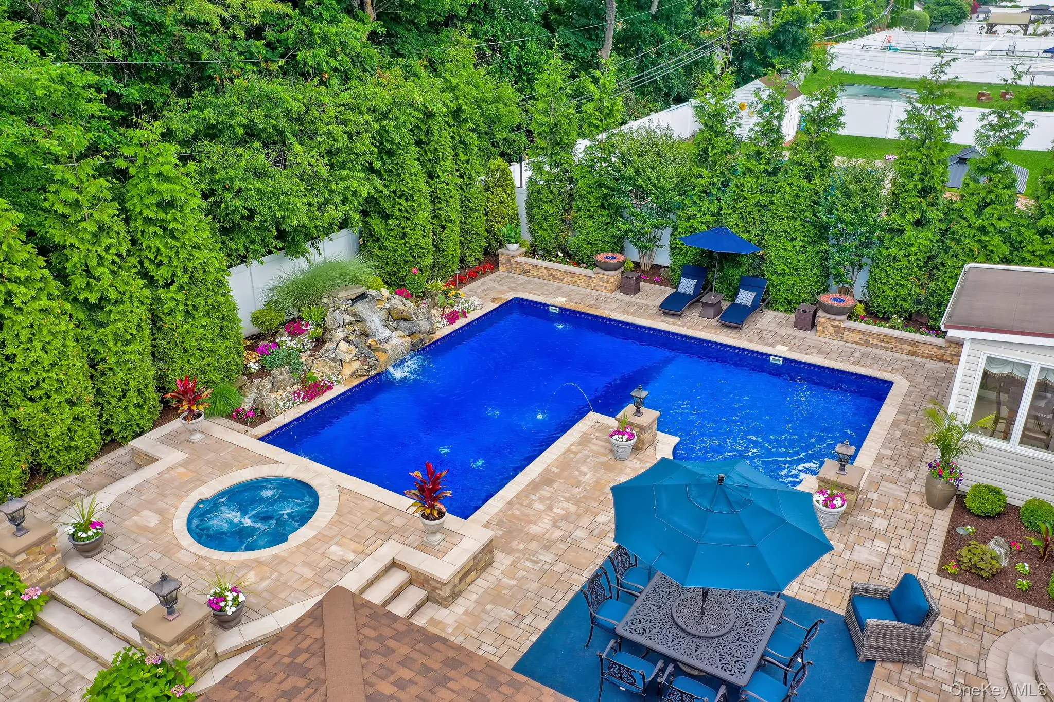 Expansive outdoor living area featuring a custom-shaped swimming pool with an integrated spa, surrounded by paver patio surfacing Expansive outdoor living area featuring a custom-shaped swimming pool with an integrated spa, surrounded by paver patio surfacing
