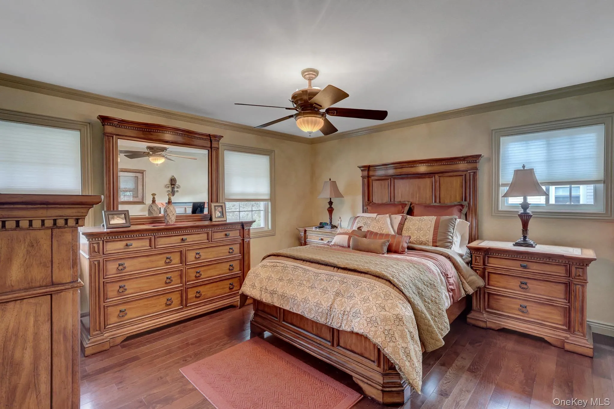 Bedroom featuring rich wood-finish flooring, a ceiling fan with integrated lighting, and multiple windows with blinds Bedroom featuring rich wood-finish flooring, a ceiling fan with integrated lighting, and multiple windows with blinds