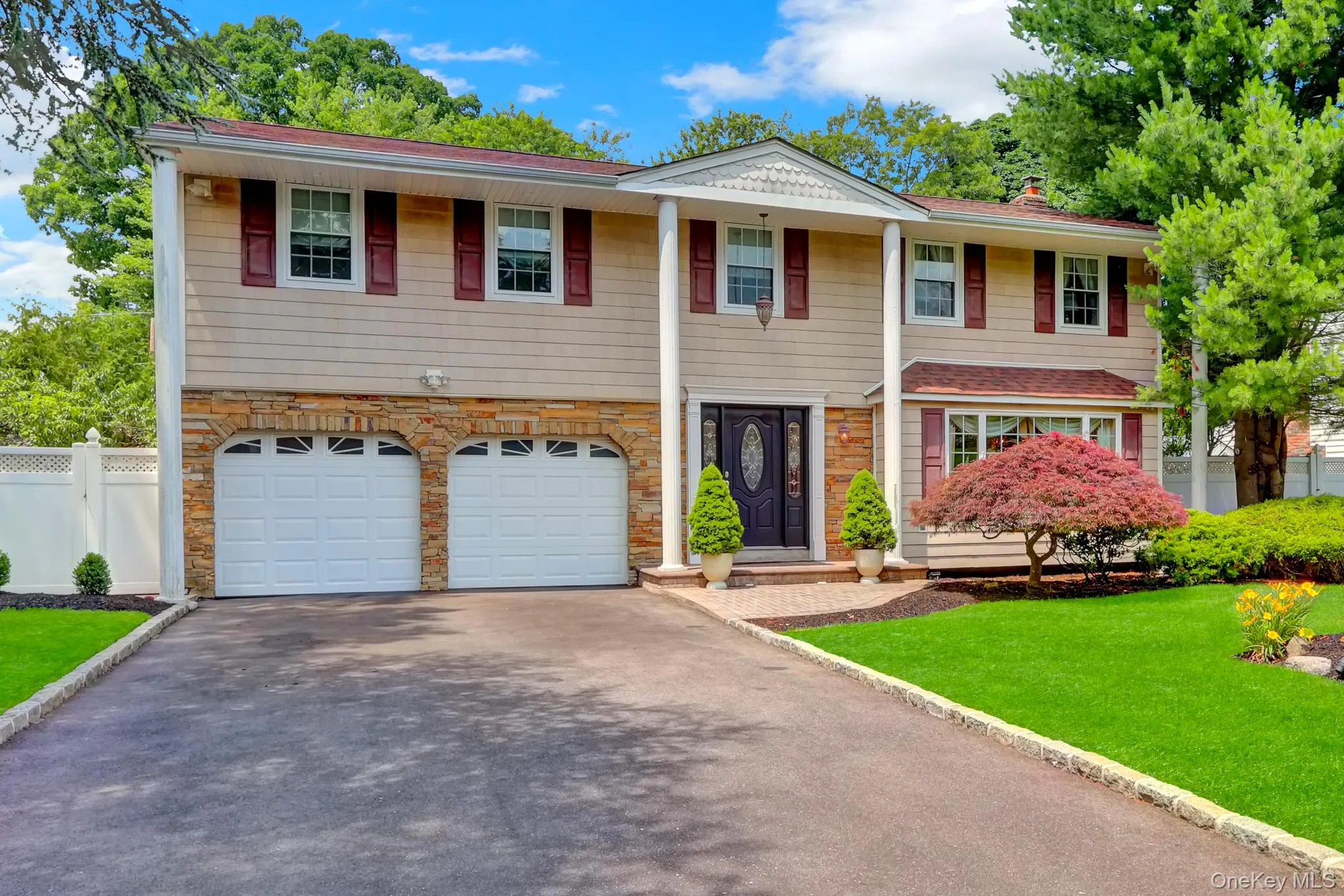 Large Colonial residence featuring a two-car garage with arched stone accents, an asphalt driveway, and a manicured lawn Large Colonial residence featuring a two-car garage with arched stone accents, an asphalt driveway, and a manicured lawn