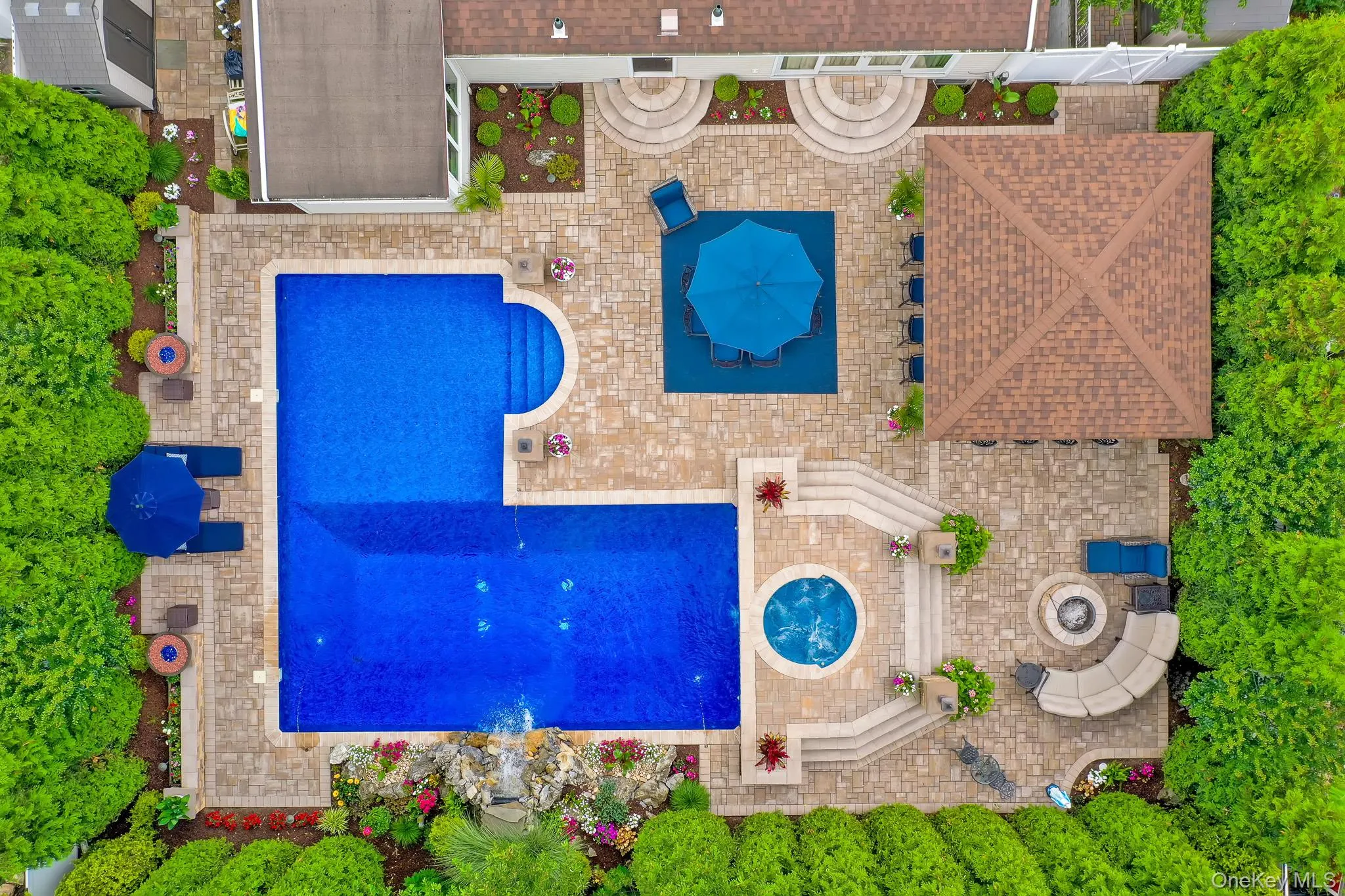 Expansive backyard featuring a large L-shaped swimming pool with integrated steps, a circular spa, and a stone waterfall feature Expansive backyard featuring a large L-shaped swimming pool with integrated steps, a circular spa, and a stone waterfall feature