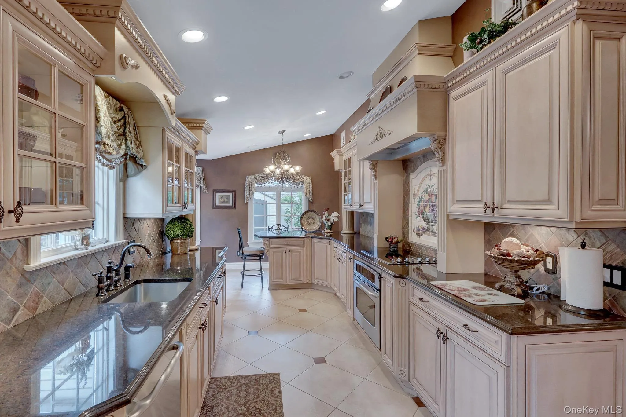 Galley kitchen featuring light-toned cabinetry, dark stone countertops, stainless steel appliances, a tile backsplash, and recessed lighting Galley kitchen featuring light-toned cabinetry, dark stone countertops, stainless steel appliances, a tile backsplash, and recessed lighting