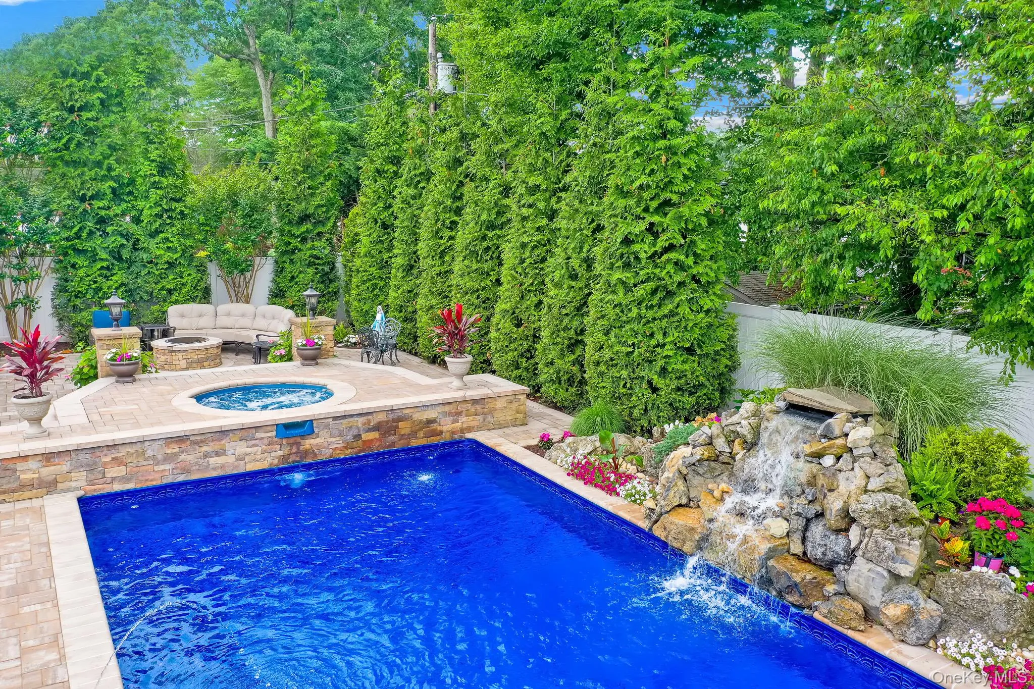 Backyard oasis featuring a sparkling blue swimming pool with a stone waterfall, integrated hot tub, and a surrounding paver patio Backyard oasis featuring a sparkling blue swimming pool with a stone waterfall, integrated hot tub, and a surrounding paver patio
