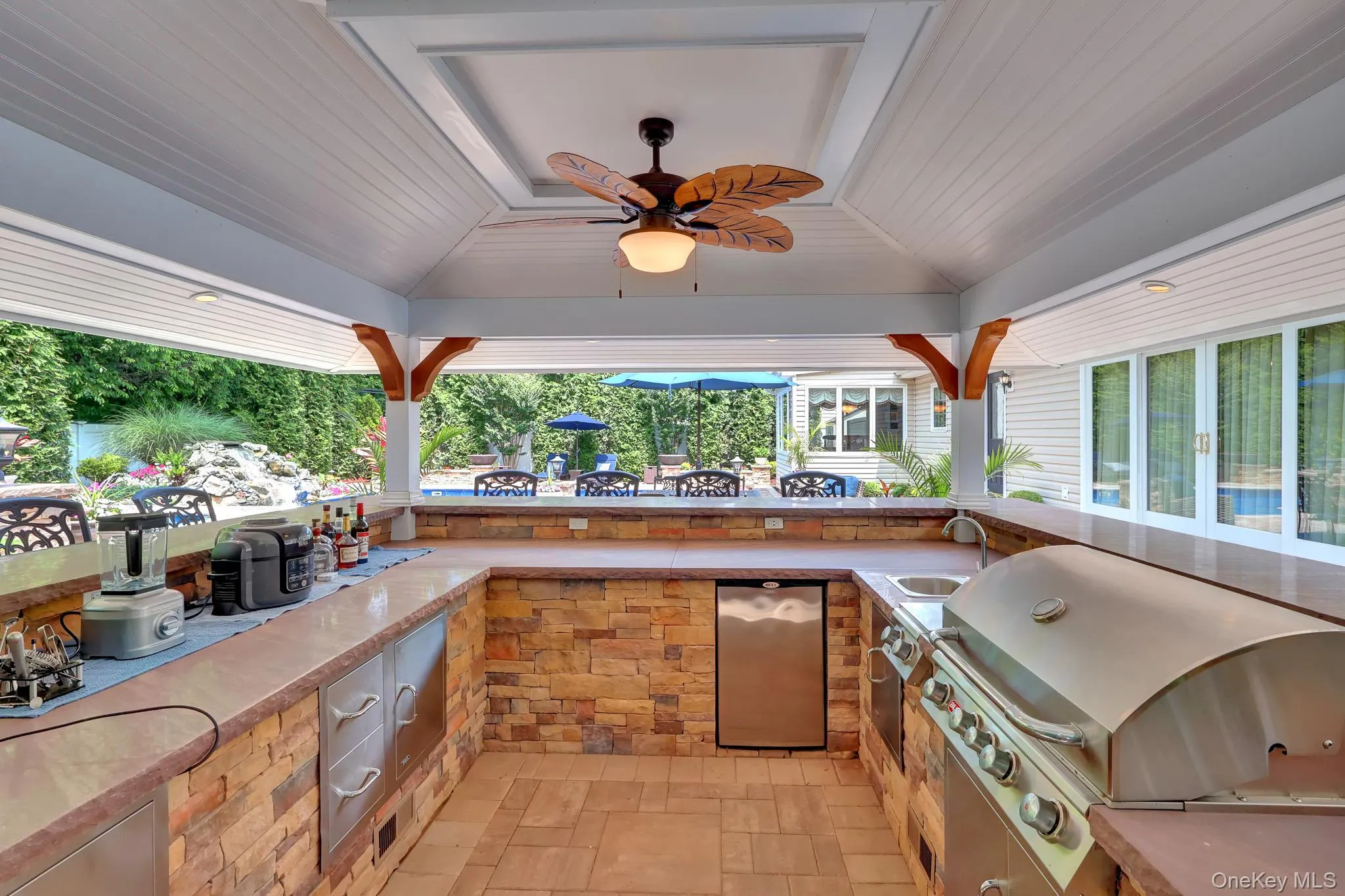 Outdoor kitchen featuring a built-in stainless steel grill, integrated sink, and under-counter refrigerator Outdoor kitchen featuring a built-in stainless steel grill, integrated sink, and under-counter refrigerator
