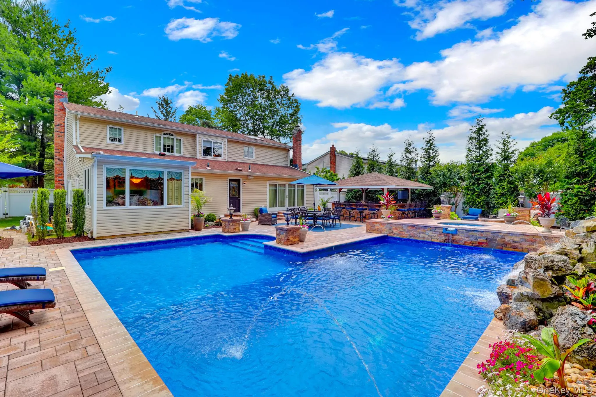 Expansive outdoor living area featuring a rectangular swimming pool, paver patio, integrated spa, and an outdoor pavilion with a built-in bar Expansive outdoor living area featuring a rectangular swimming pool, paver patio, integrated spa, and an outdoor pavilion with a built-in bar