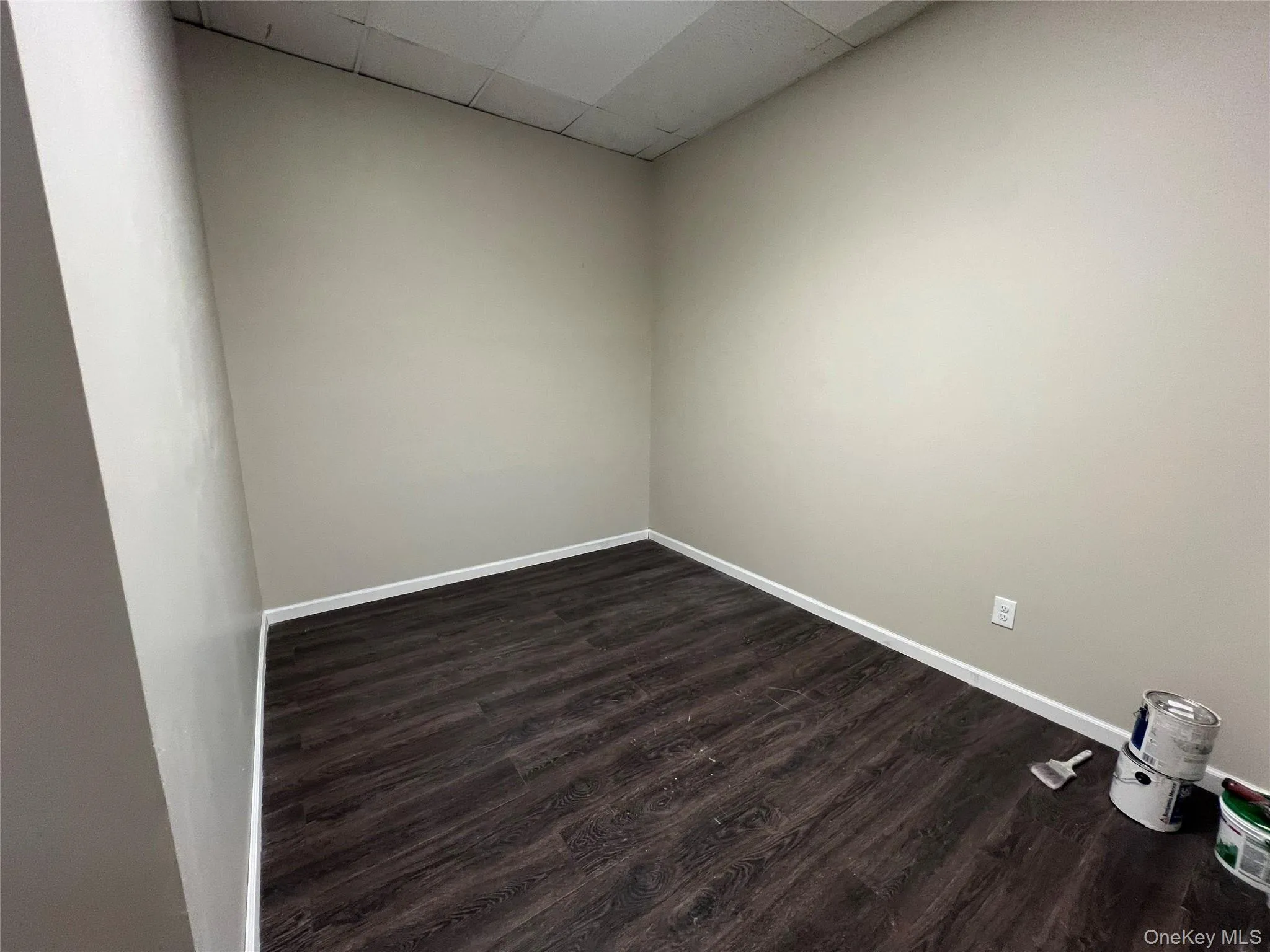 Empty room featuring a drop ceiling, dark wood-type flooring, and baseboards Empty room featuring a drop ceiling, dark wood-type flooring, and baseboards