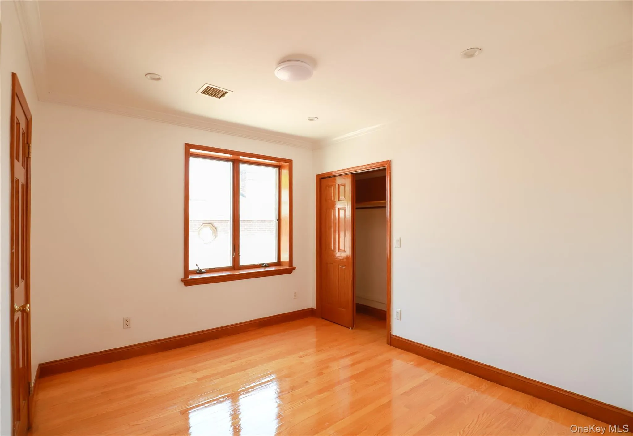 Room featuring hardwood flooring, a multi-pane window with wood trim, crown molding, and a closet with bifold wood doors Room featuring hardwood flooring, a multi-pane window with wood trim, crown molding, and a closet with bifold wood doors