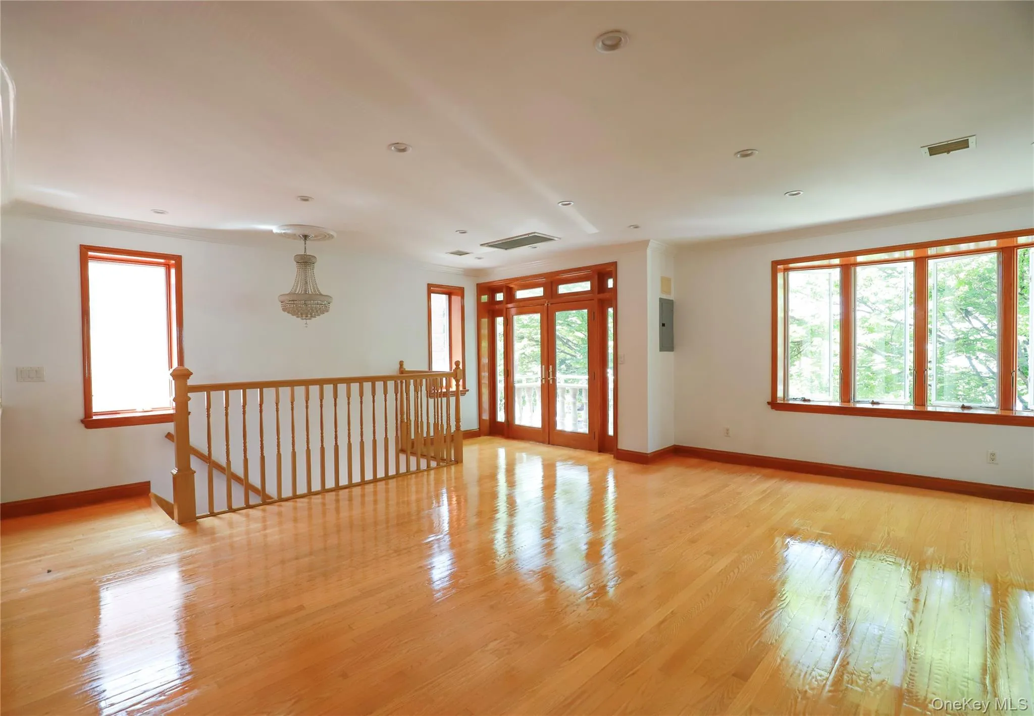 Spacious open area featuring high-gloss wood-finish flooring, abundant natural light from multiple windows, and a decorative chandelier Spacious open area featuring high-gloss wood-finish flooring, abundant natural light from multiple windows, and a decorative chandelier