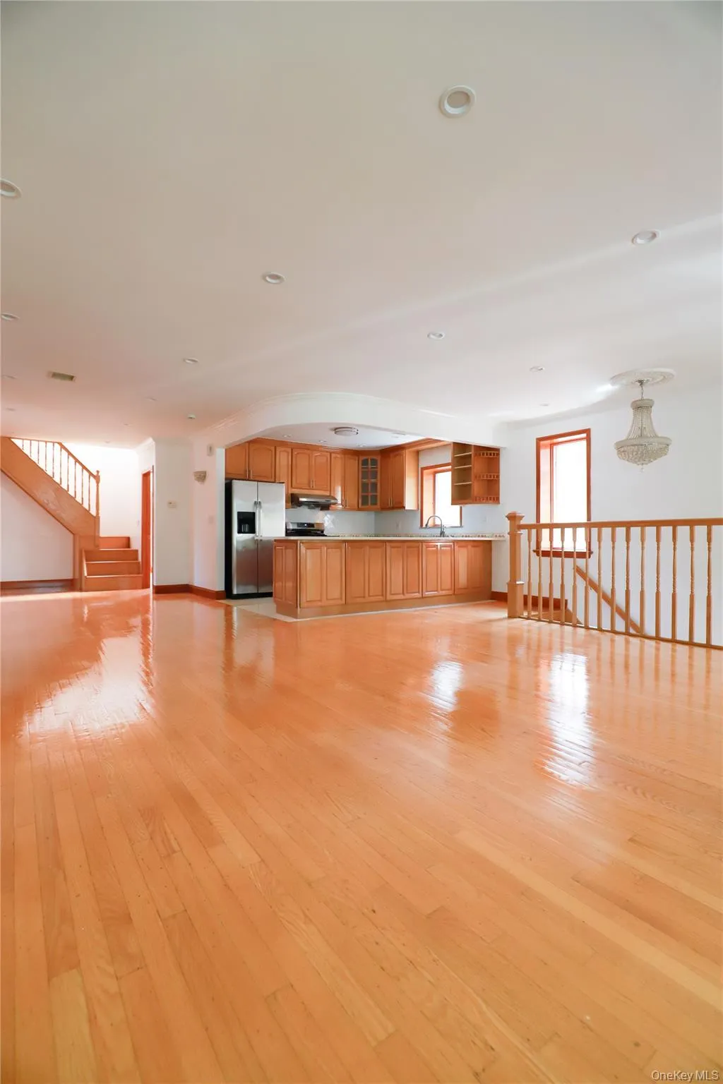 Expansive open-concept space featuring polished wood flooring, a kitchen with wood cabinetry, stainless steel appliances, recessed lighting, and a chandelier Expansive open-concept space featuring polished wood flooring, a kitchen with wood cabinetry, stainless steel appliances, recessed lighting, and a chandelier