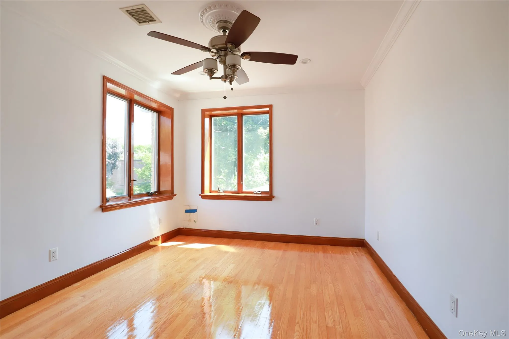 Bright interior space featuring wood-finish flooring, two large windows with wood trim, and a ceiling fan with integrated lighting Bright interior space featuring wood-finish flooring, two large windows with wood trim, and a ceiling fan with integrated lighting