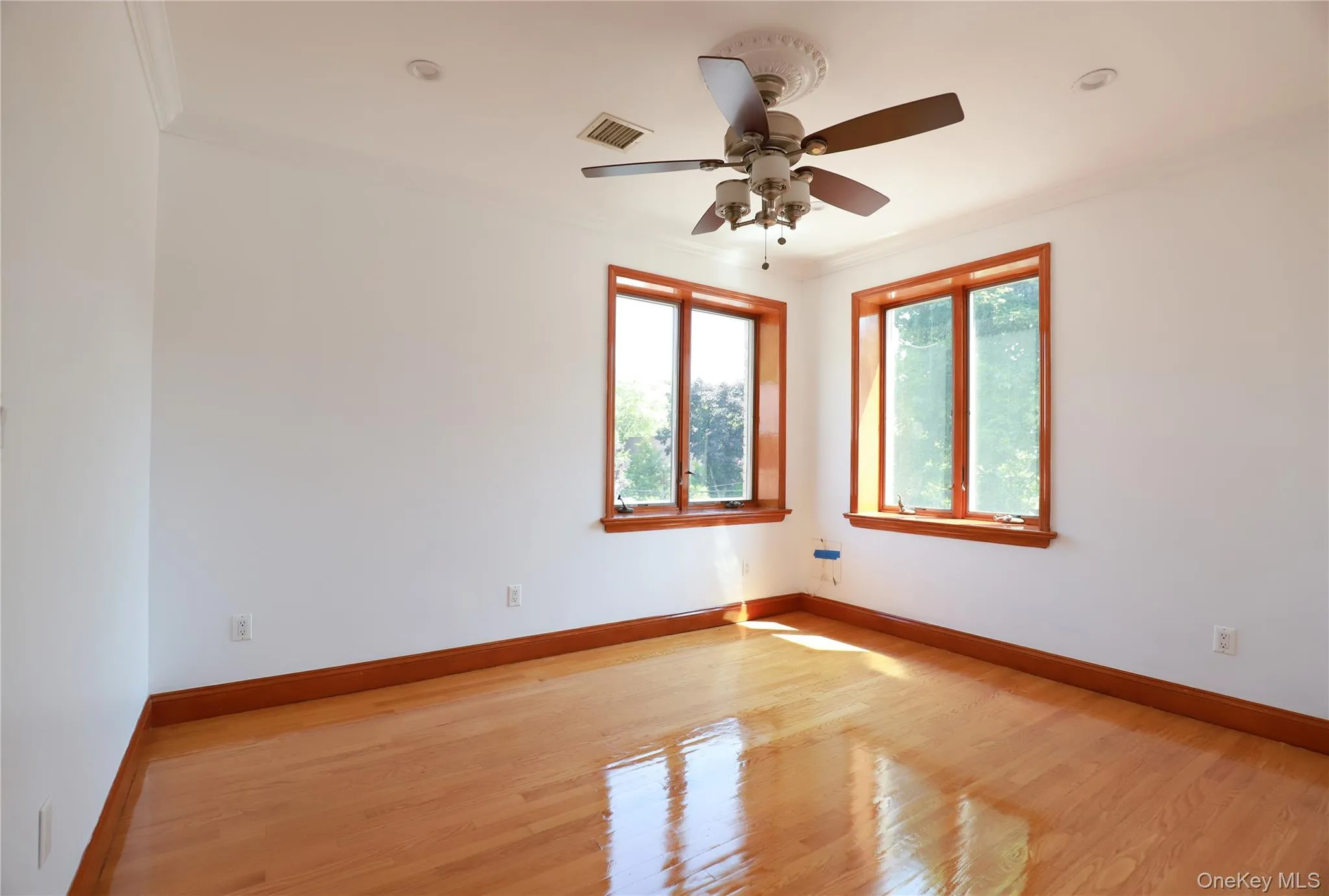 Bright room featuring warm wood-finish flooring, white walls, and crown molding Bright room featuring warm wood-finish flooring, white walls, and crown molding