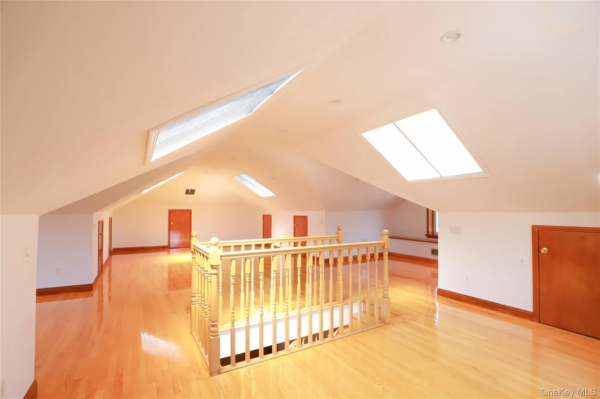 Spacious upper-level area featuring abundant natural light from multiple skylights, warm wood-finish flooring, and a light wood railing overlooking the lower level Spacious upper-level area featuring abundant natural light from multiple skylights, warm wood-finish flooring, and a light wood railing overlooking the lower level